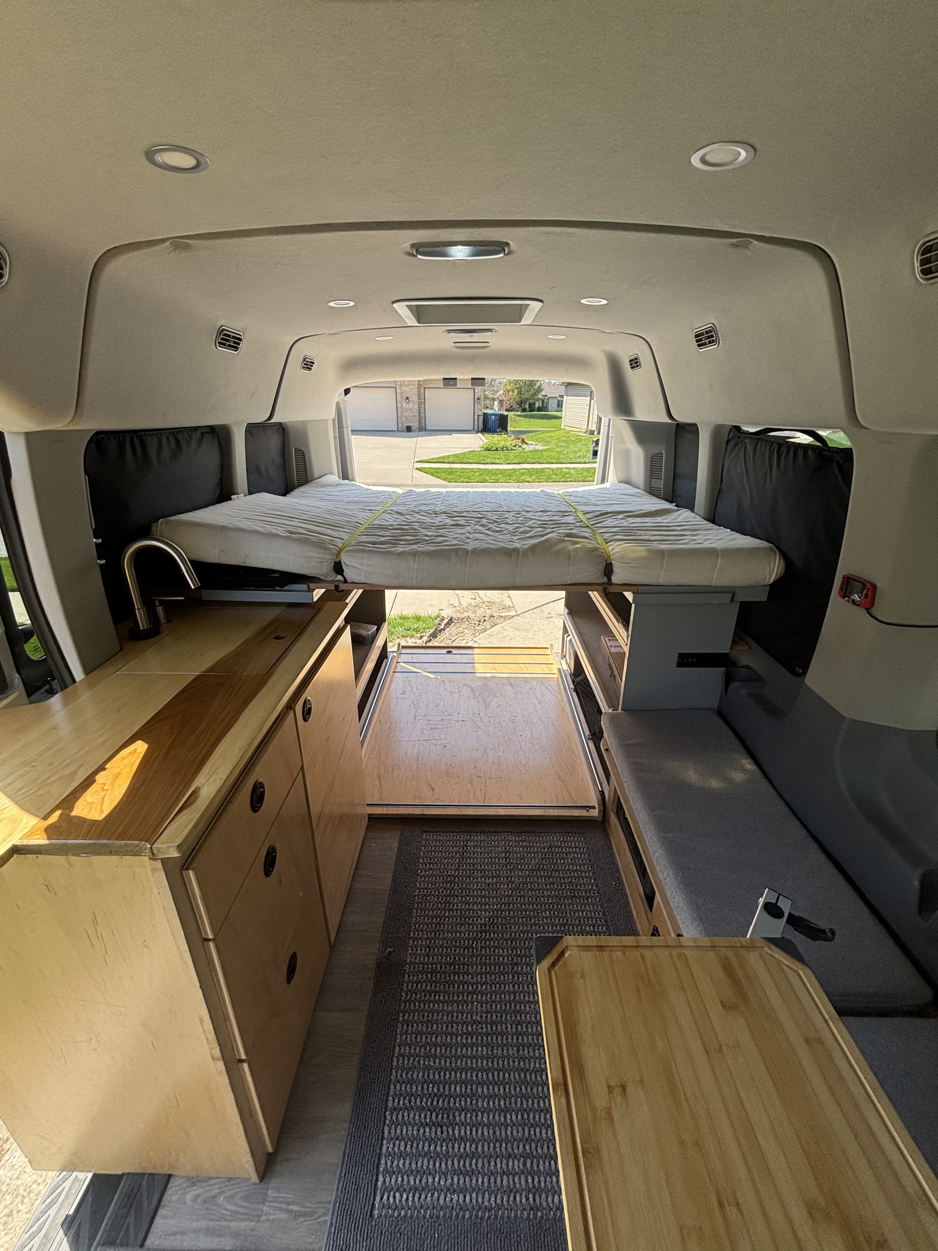 This RV rental interior showcases a custom camper van with an elevated bed, kitchenette, bench seating, and storage, ready for adventure.. Ford Transit 2015