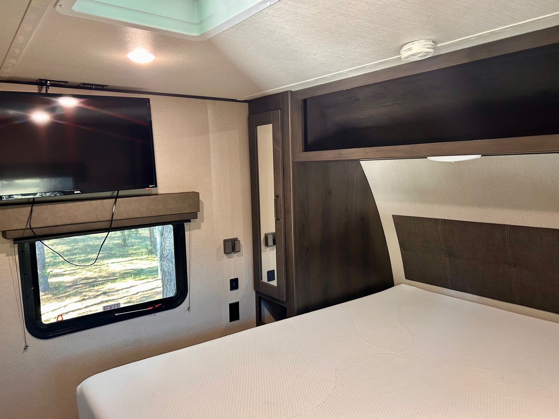RV rental bedroom: comfortable bed with white mattress, TV, window revealing trees, and convenient storage cabinets.. Grand Design Transcend Xplor 2022