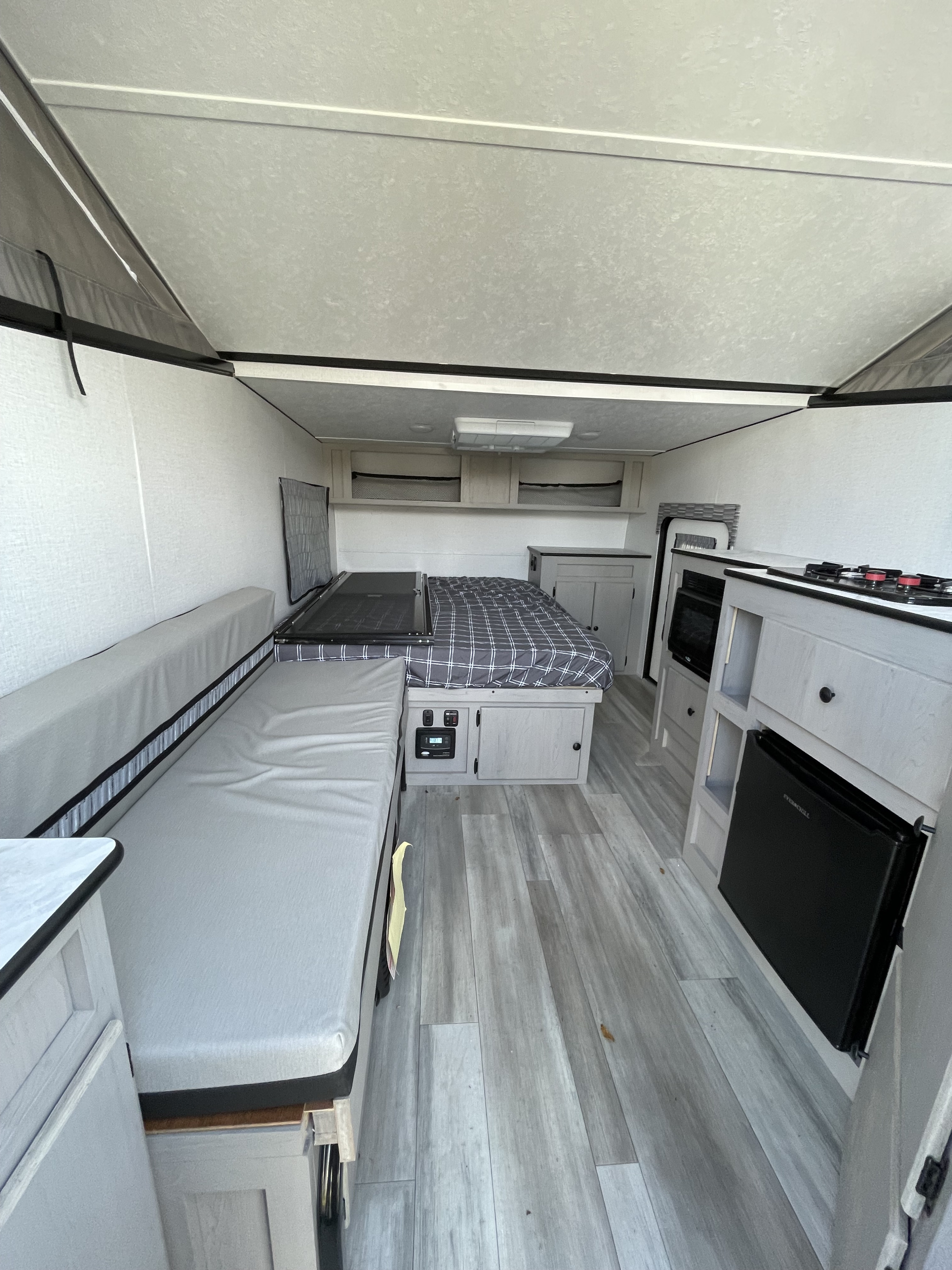 Experience comfort in this RV rental interior: cozy bed, long sofa, and a compact kitchen with stove, microwave, and mini-fridge.. Forest River Viking LS 2024