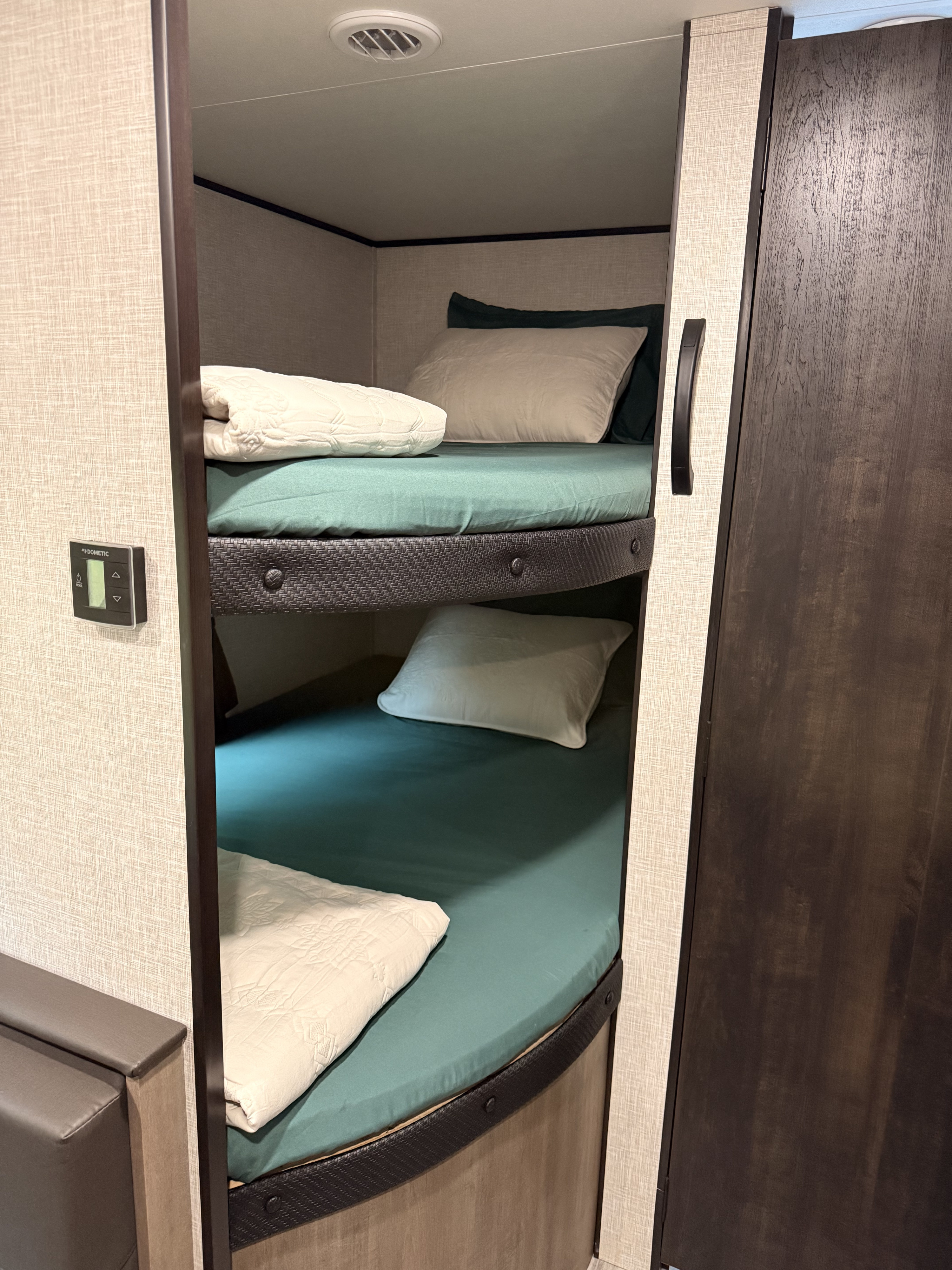 RV rental: two bunk beds with green sheets, white pillows/blankets, a Dometic control panel, and a wood-paneled door.. Jayco Jay Flight SLX 2024