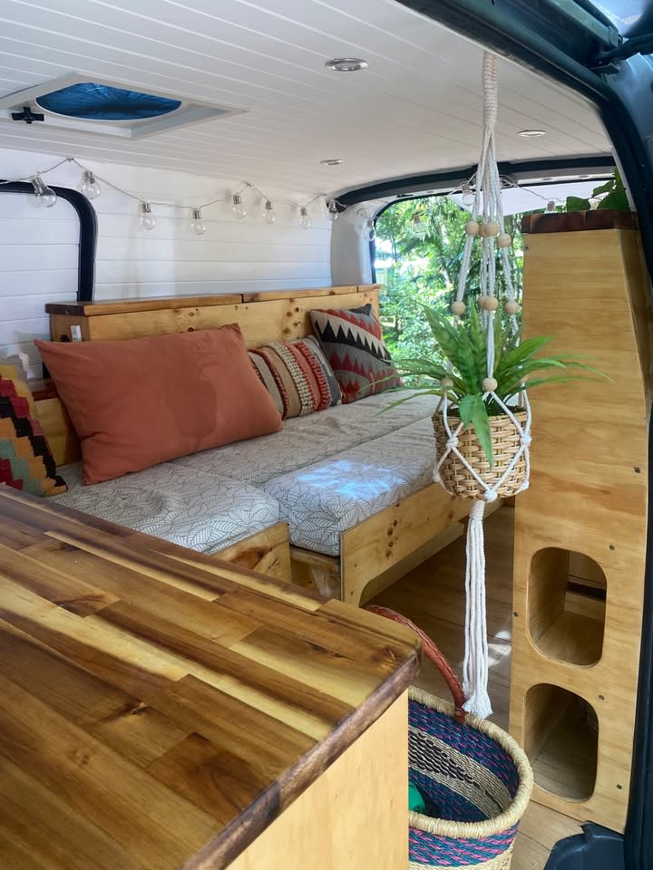 Cozy rv rental interior. Wooden bed, countertop, macrame plant, & string lights create a bright, inviting space for adventure.. Hyundai Kickback Camper 2011