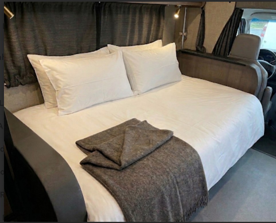 Cozy, well-made bed in an RV rental, featuring crisp white bedding and a warm grey blanket, ready for comfortable travel.. Wayfarer Wayfarer Motorhome 2020