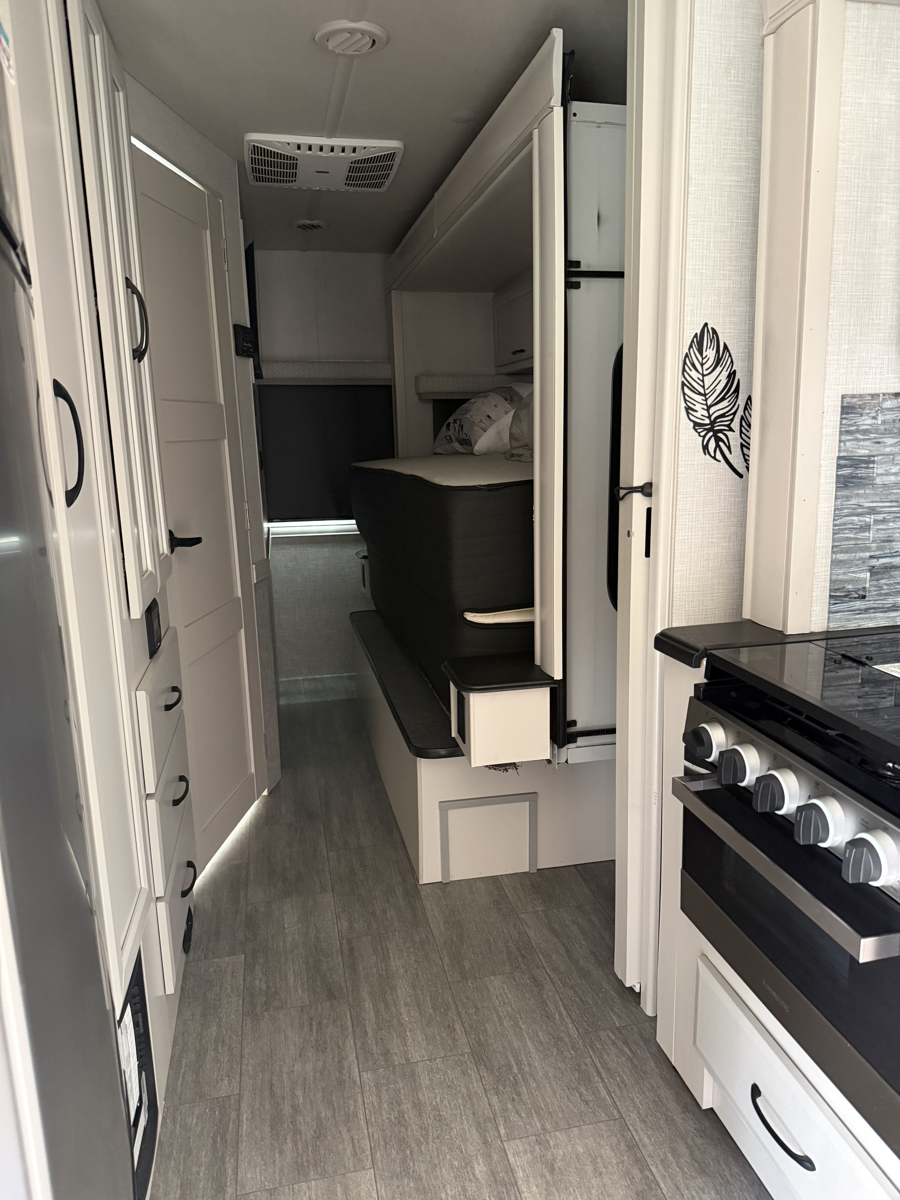 This rv rental interior features a clean hallway leading to a cozy bedroom, with a modern kitchenette on the right.. Holiday Rambler Admiral 2024