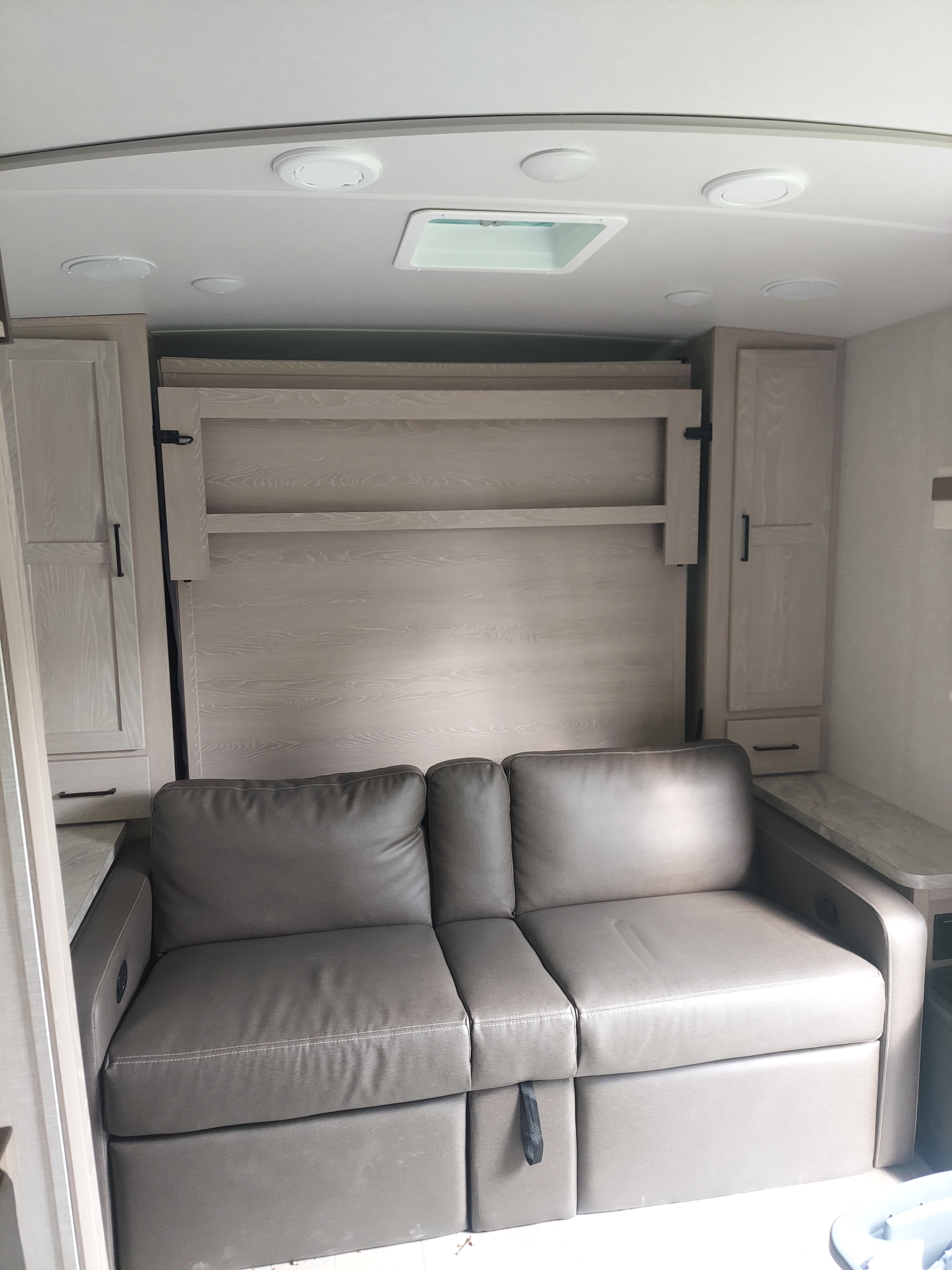 Inside an RV rental: A stylish gray sofa, folded murphy bed, light cabinets, and ceiling lights/vent for compact living.. Forest River Rockwood Mini Lite 2021