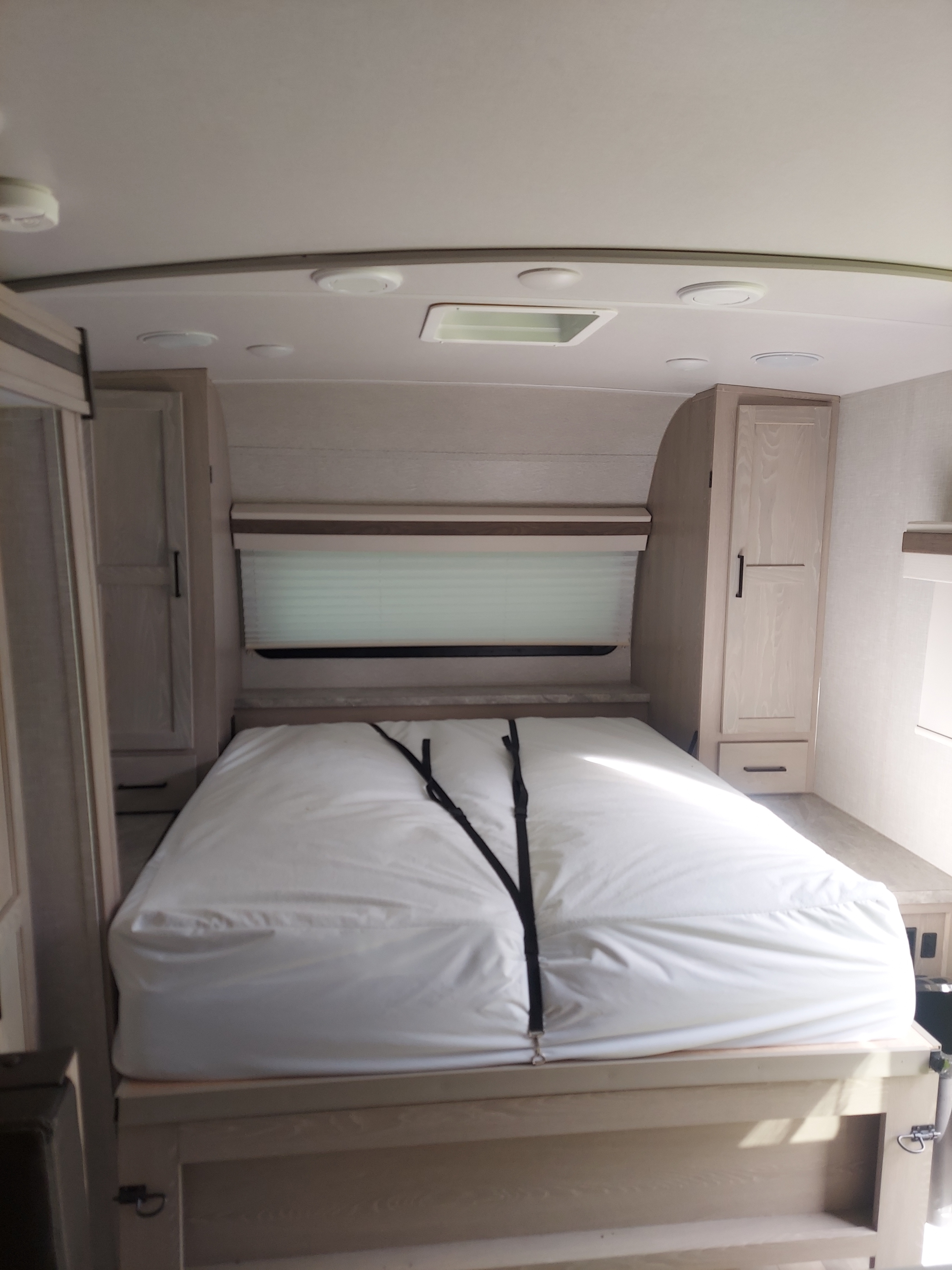 RV rental bedroom with a neatly made bed, white bedding secured by straps, window with blinds, and light-colored cabinets.. Forest River Rockwood Mini Lite 2021