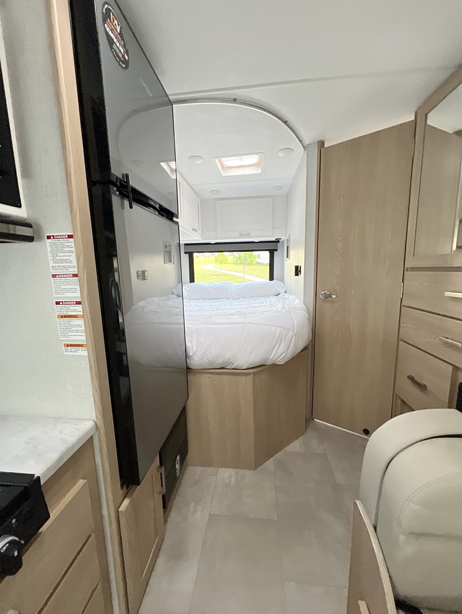 RV rental: Bright interior featuring a compact bedroom with a white-covered bed, window, side fridge, and light wood cabinets.. Thor Freedom Elite 2026