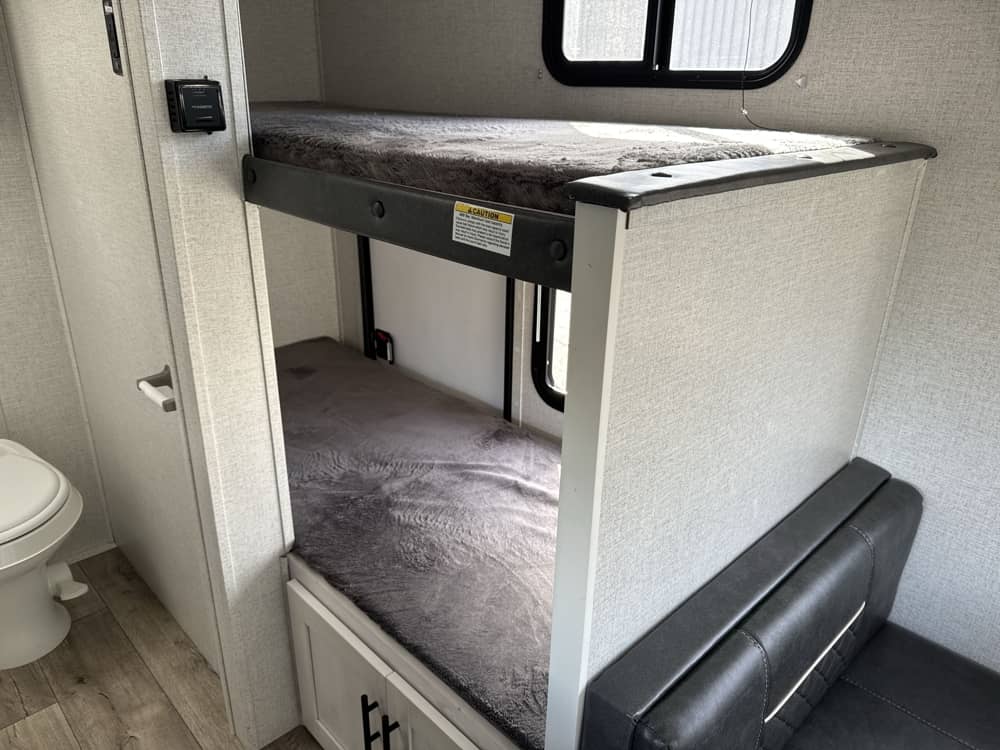 RV rental interior featuring cozy bunk beds, a toilet, and seating area. Perfect for family adventures in your rental RV.. Dutchmen Coleman Rubicon 2023