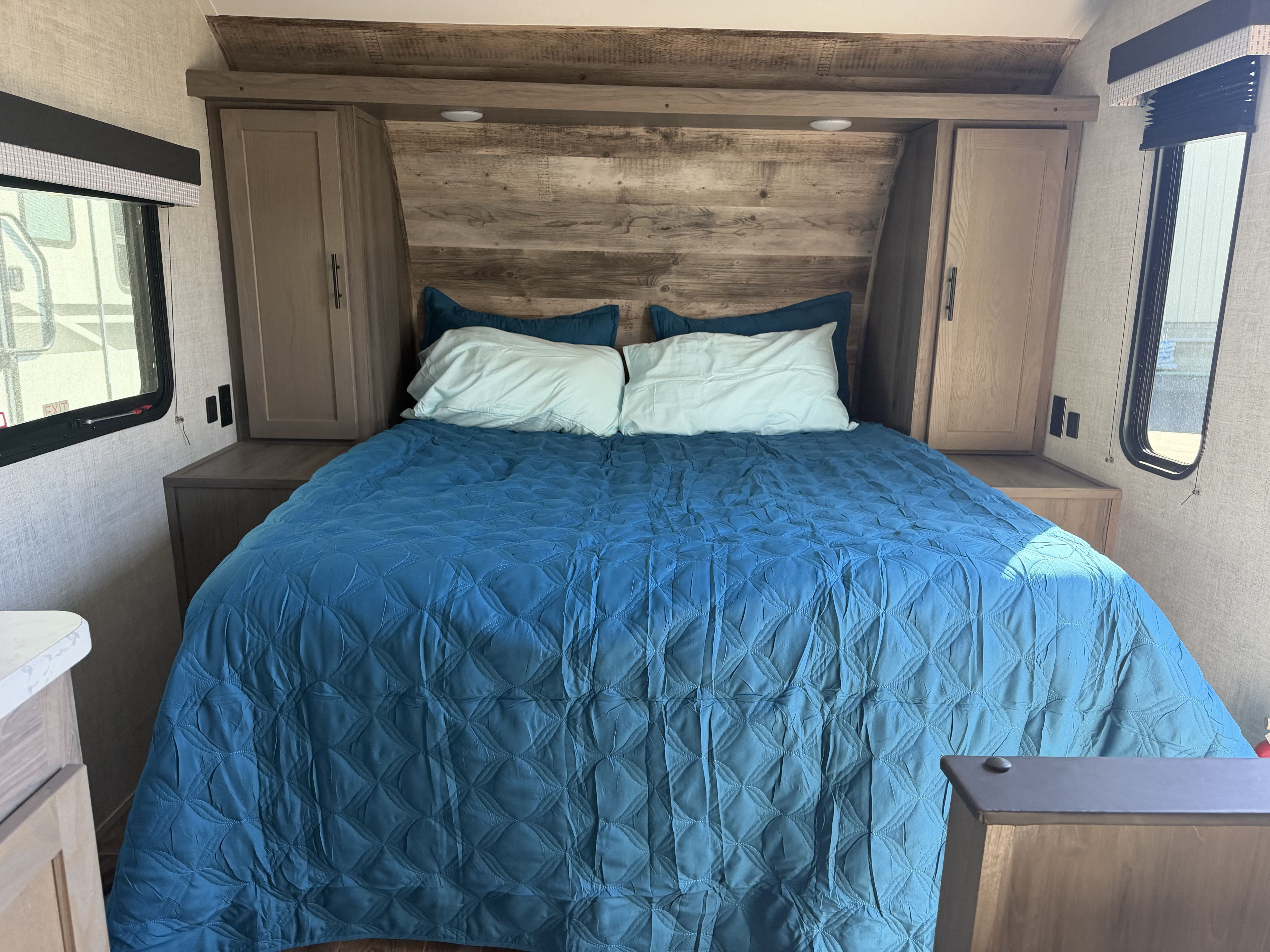 RV rental bedroom interior: blue quilted bed, light pillows, rustic wood headboard, storage cabinets & side windows.. Gulf Stream Ameri-Lite Super Lite 2022