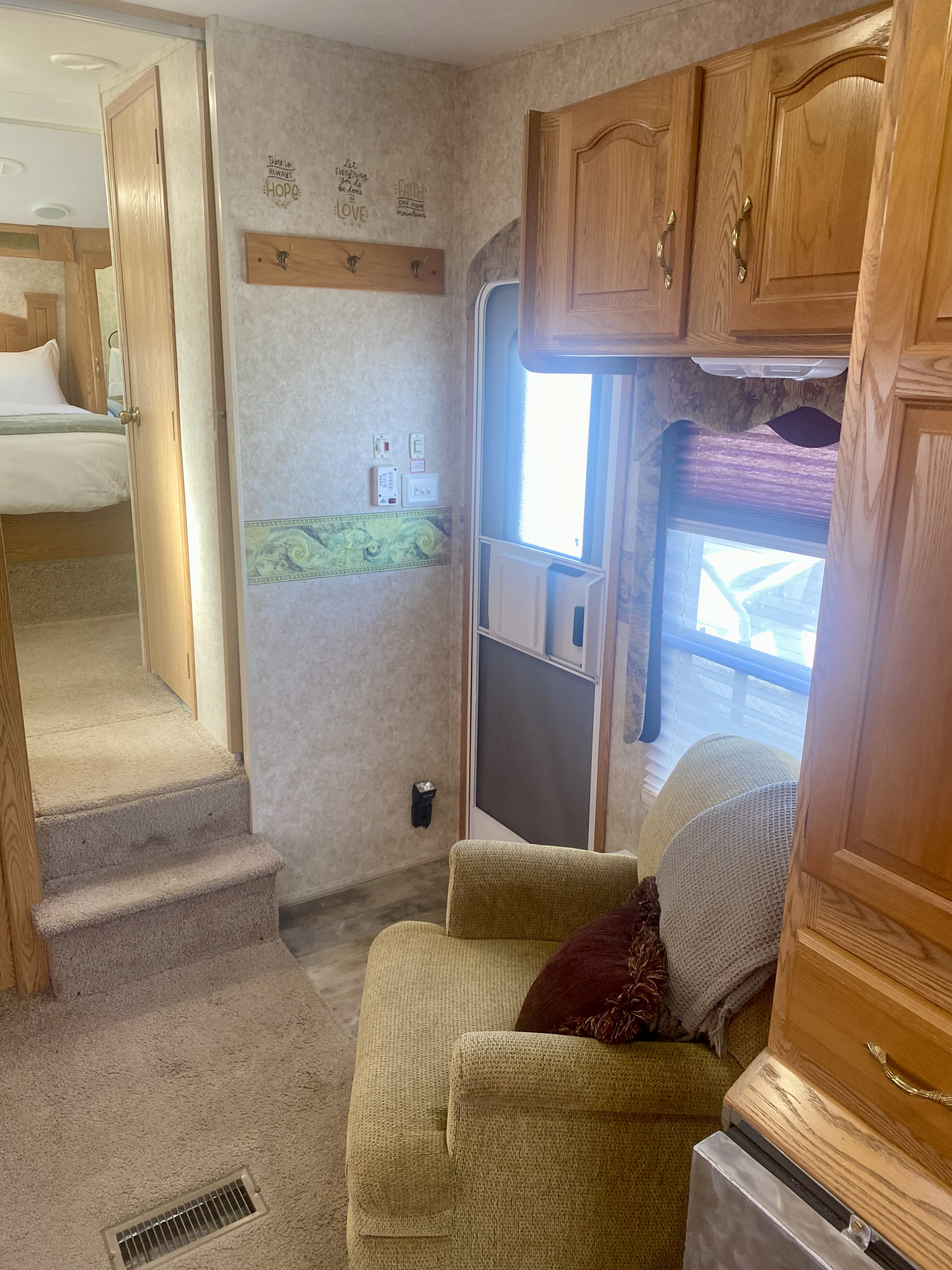 RV rental interior view: a cozy living area with an armchair and cabinets, connected to a raised bedroom by carpeted steps.. Keystone RV Cougar 2007