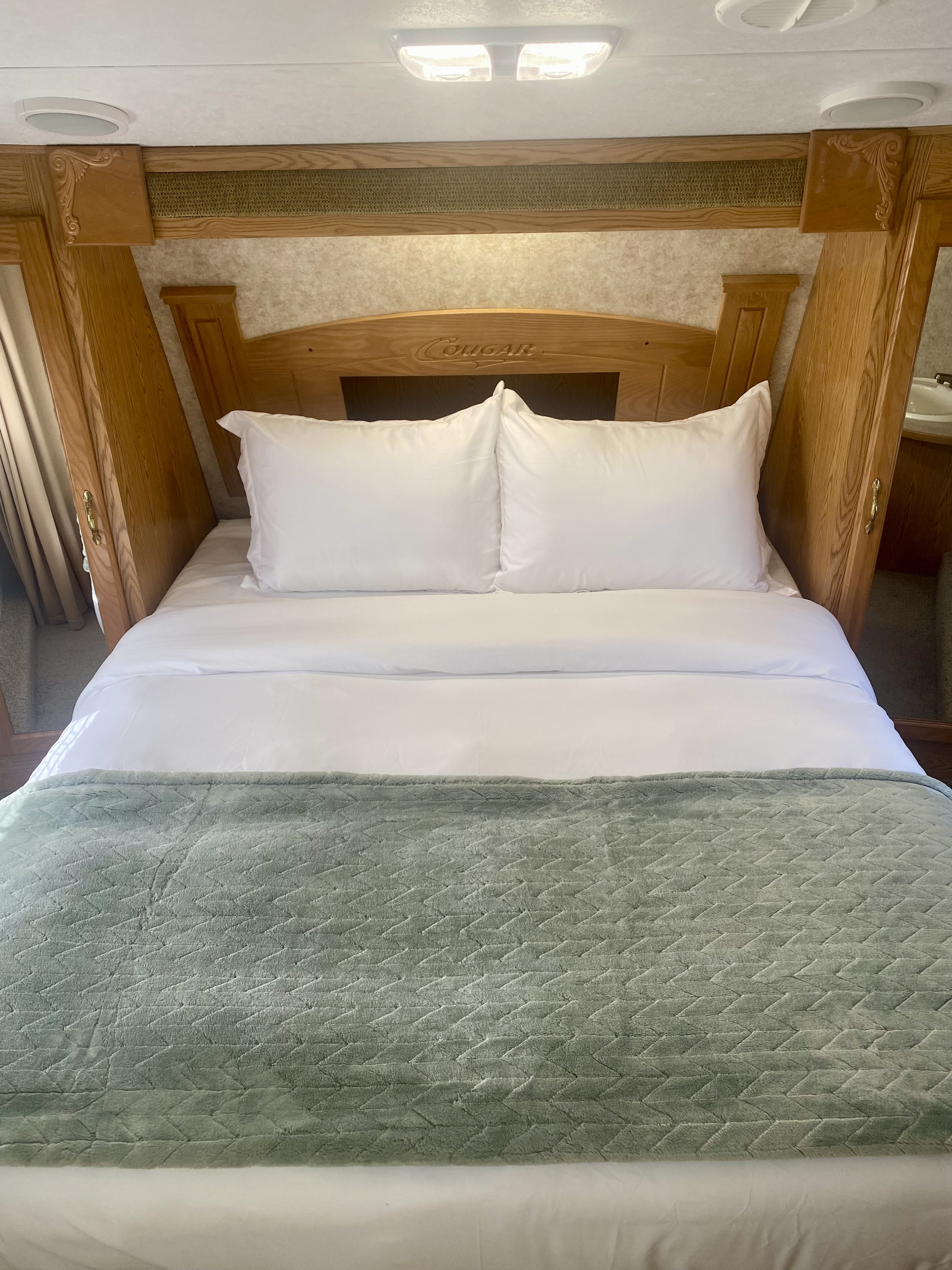 Cozy RV rental bed with fresh white linens, a textured green blanket, and a wooden headboard for comfortable travel.. Keystone RV Cougar 2007