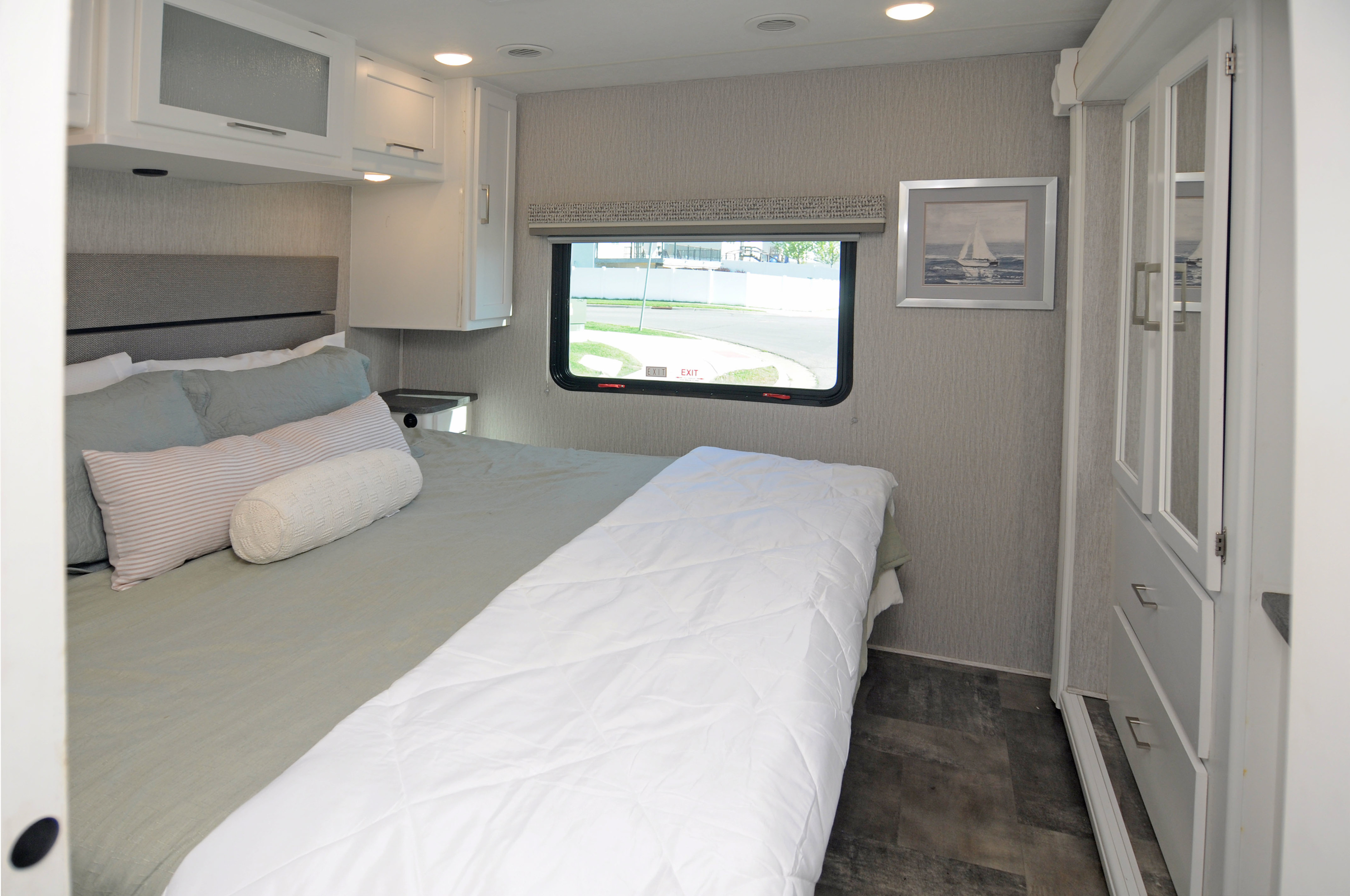 Clean and cozy RV rental bedroom with a bed, overhead cabinets, window with a view, and built-in wardrobe.. Coachmen Pursuit 2022
