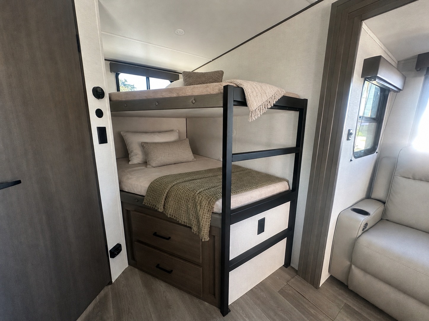 RV rental offers cozy bunk beds with storage drawers and a comfy recliner beside a window. Neutral tones fill the space.. Grand Design Transcend Xplor 2026