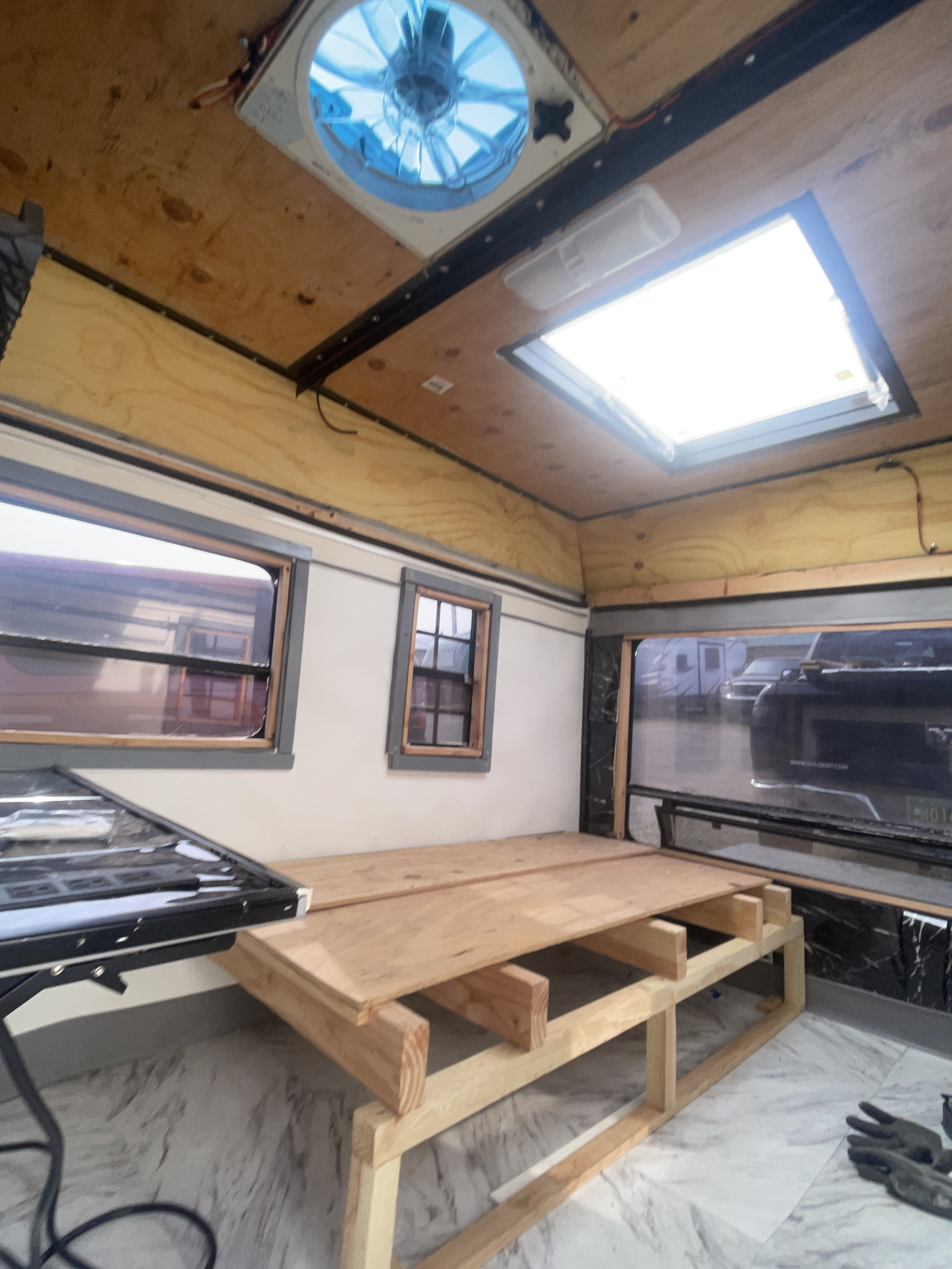 Renovating an RV rental: Inside view with new bed frame construction, windows, ceiling fan, and bright skylight.. Camping Equipment Cargo Trailer Conversion 2020