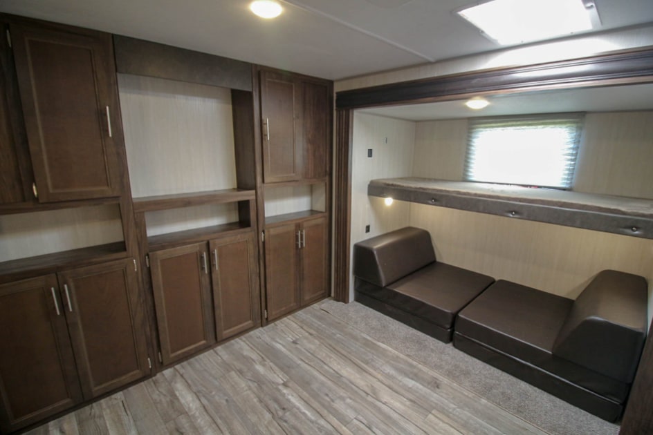 An RV rental's cozy bunkhouse area with dark wood storage, bunk bed, and two brown modular sofas.. Forest River Cherokee 2020