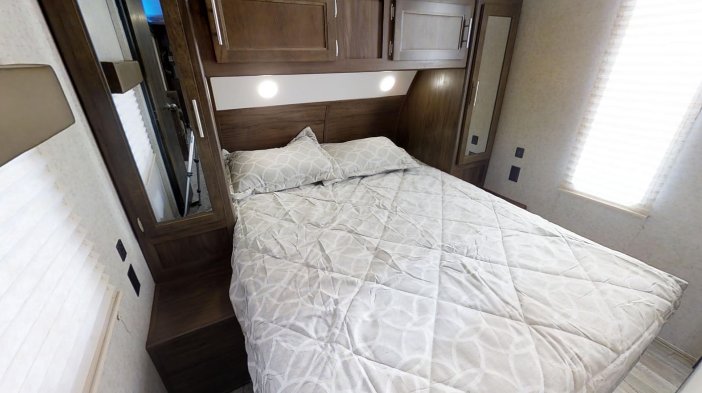 RV rental bedroom with a comfortable bed, wood storage cabinets, and bright window. Ideal for trips and travel.. Forest River Cherokee 2020