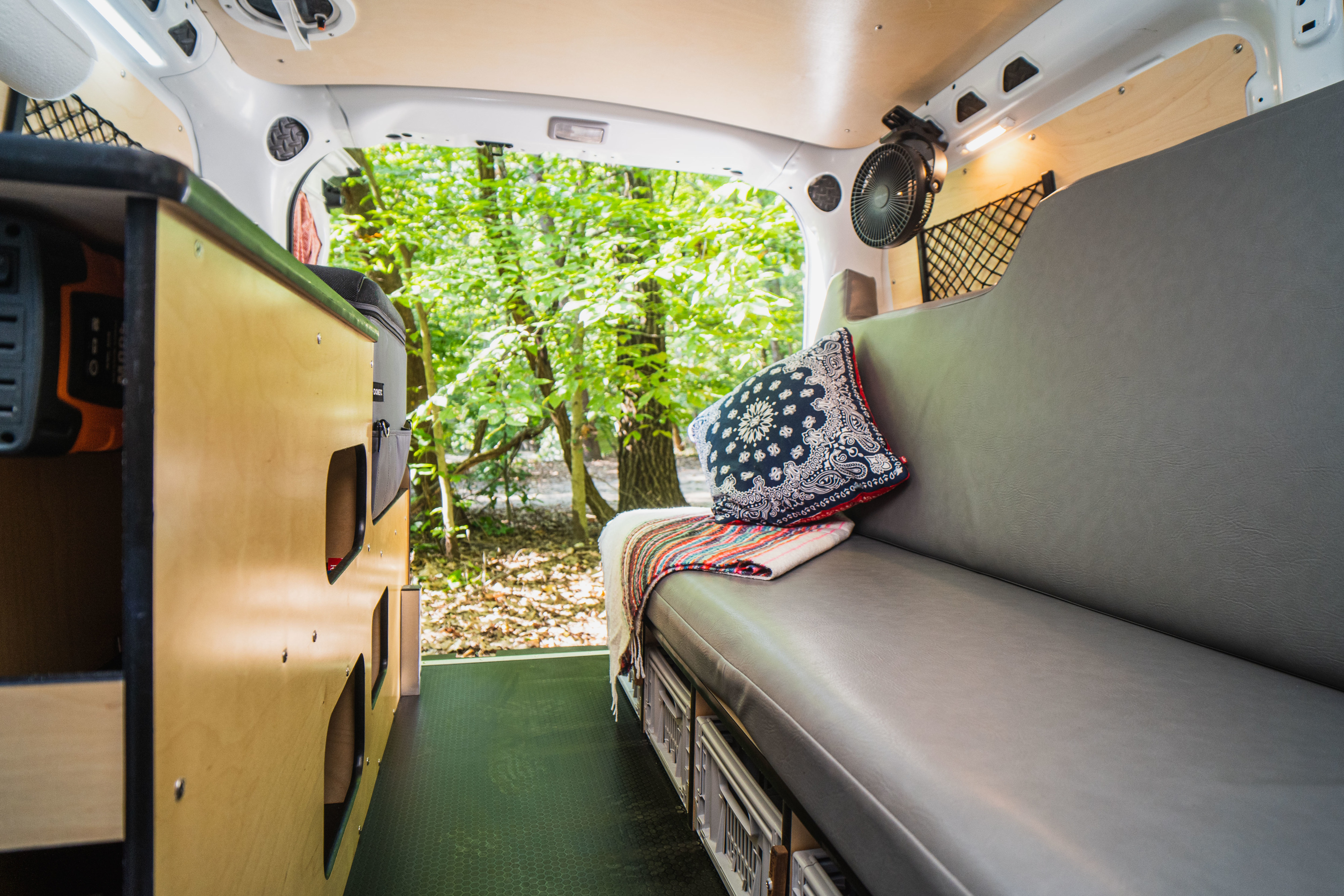 Inside a comfortable rv rental camper van, featuring a cozy bench, storage, and an inviting view of a green forest for travel.. RAM ProMaster City 2020