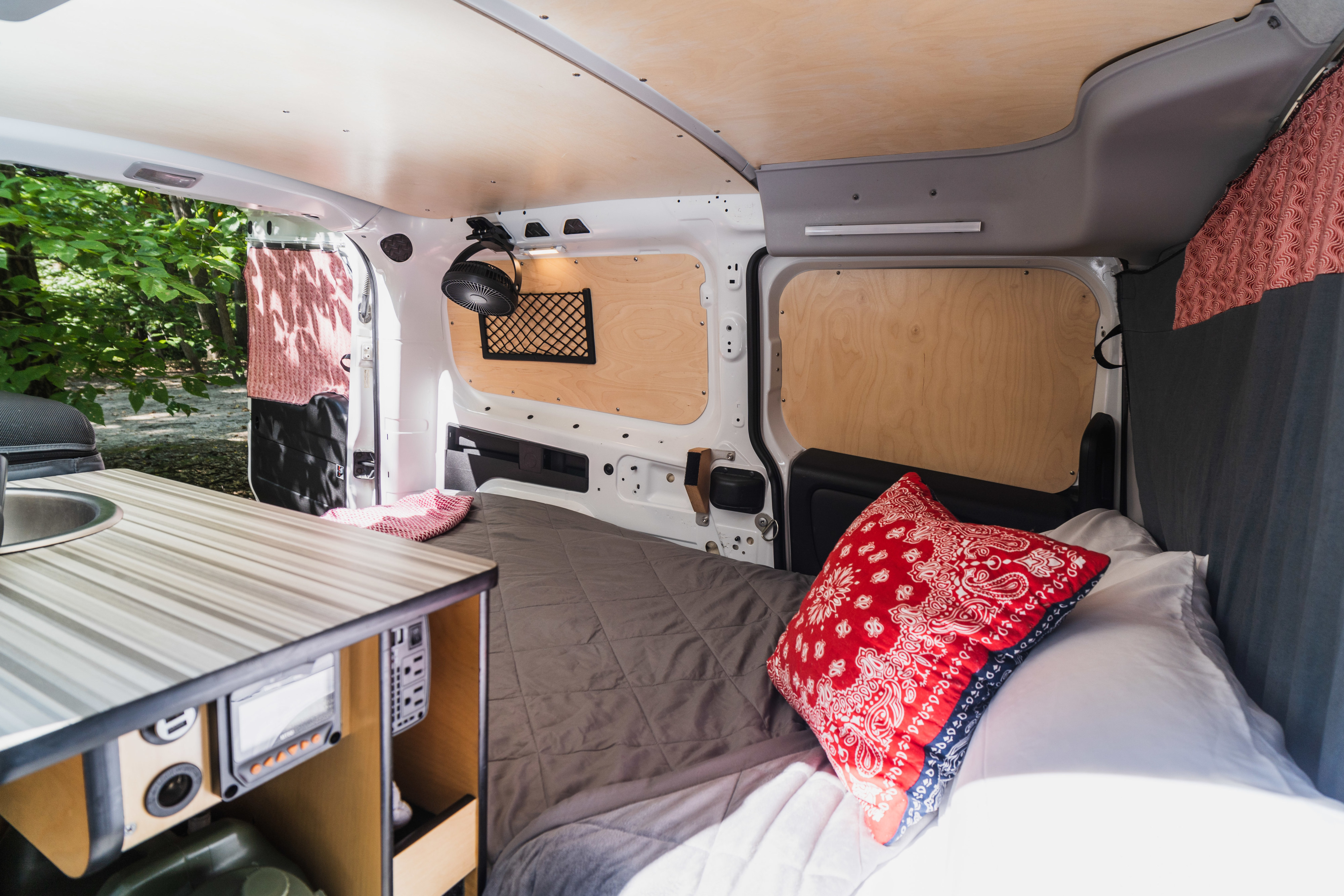 Inside a compact RV rental: a comfy bed, functional kitchen sink, and wood-paneled walls for road trip camping.. RAM ProMaster City 2020
