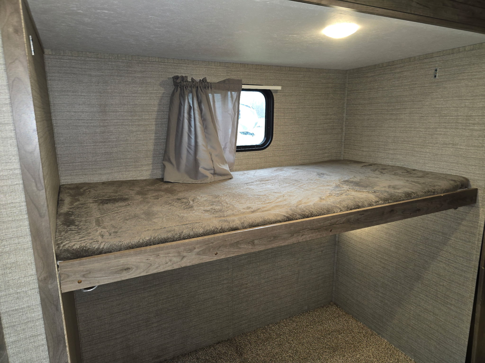 Cozy RV rental interior shows a well-lit bunk bed with a window and textured walls, providing a comfortable sleeping area.. Dutchmen Aspen Trail 2019