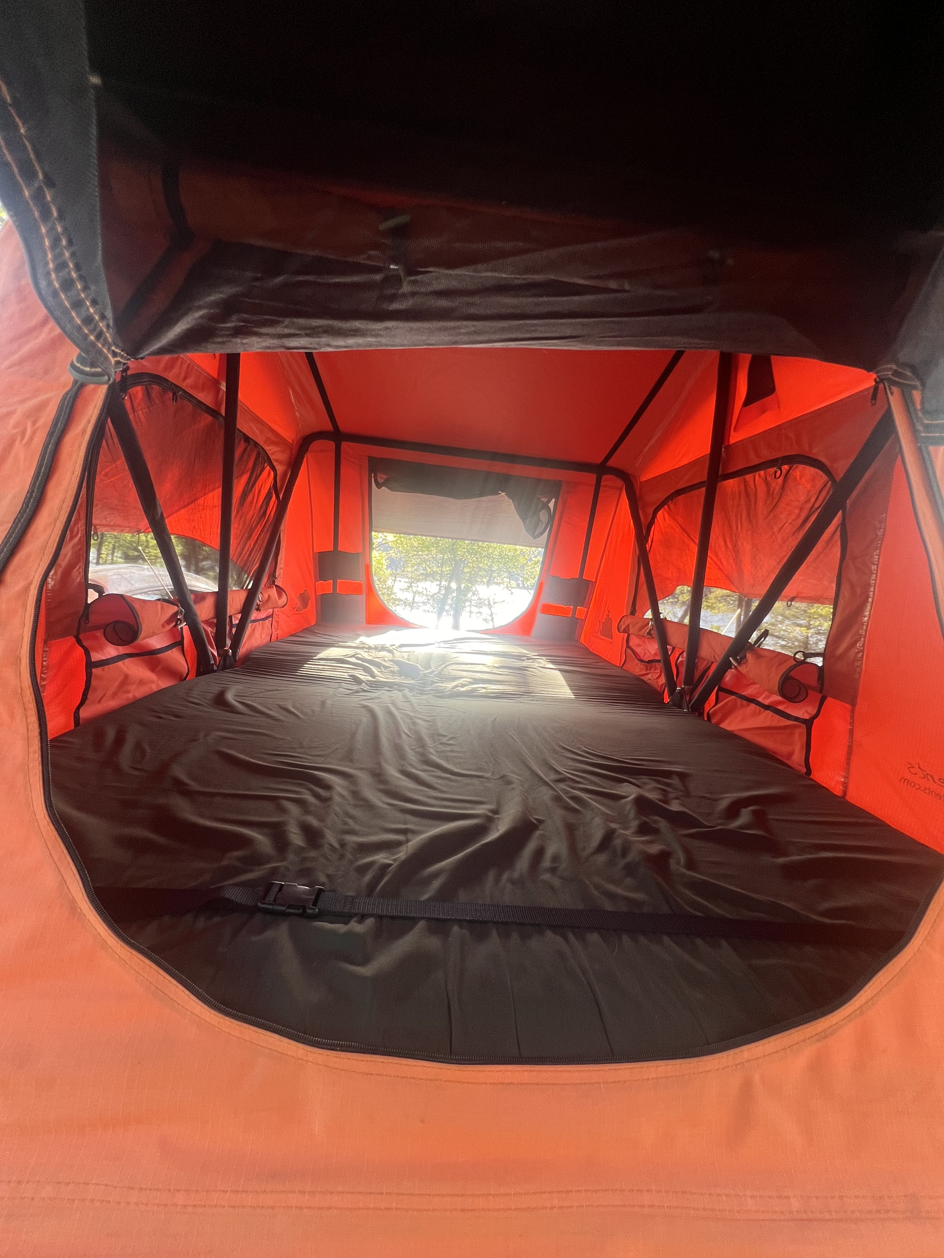 Interior of a vibrant orange rooftop tent with a dark mattress, looking out to a bright day. Ideal for your RV rental journey.. American Trailer Suburu Forester 2007
