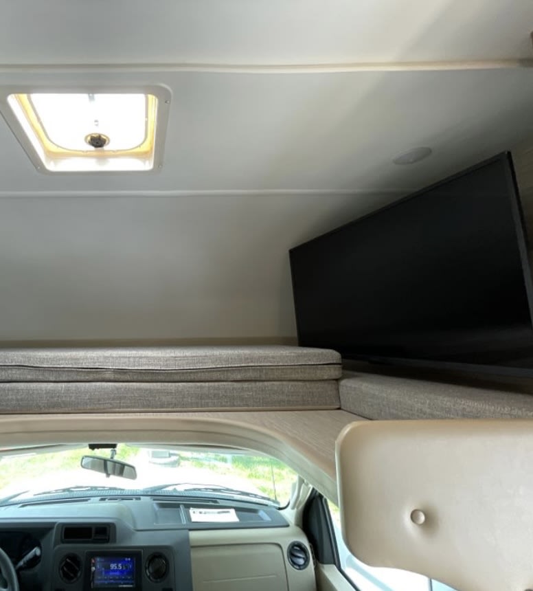 Cozy rv rental cab-over bunk with a mounted TV and skylight, perfect for comfortable travel and viewing.. Thor Coleman 2022