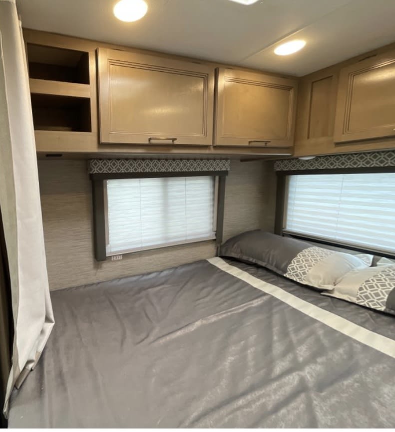 RV rental bedroom with a gray bed, two windows with blinds, and overhead storage cabinets for cozy travel.. Thor Coleman 2022