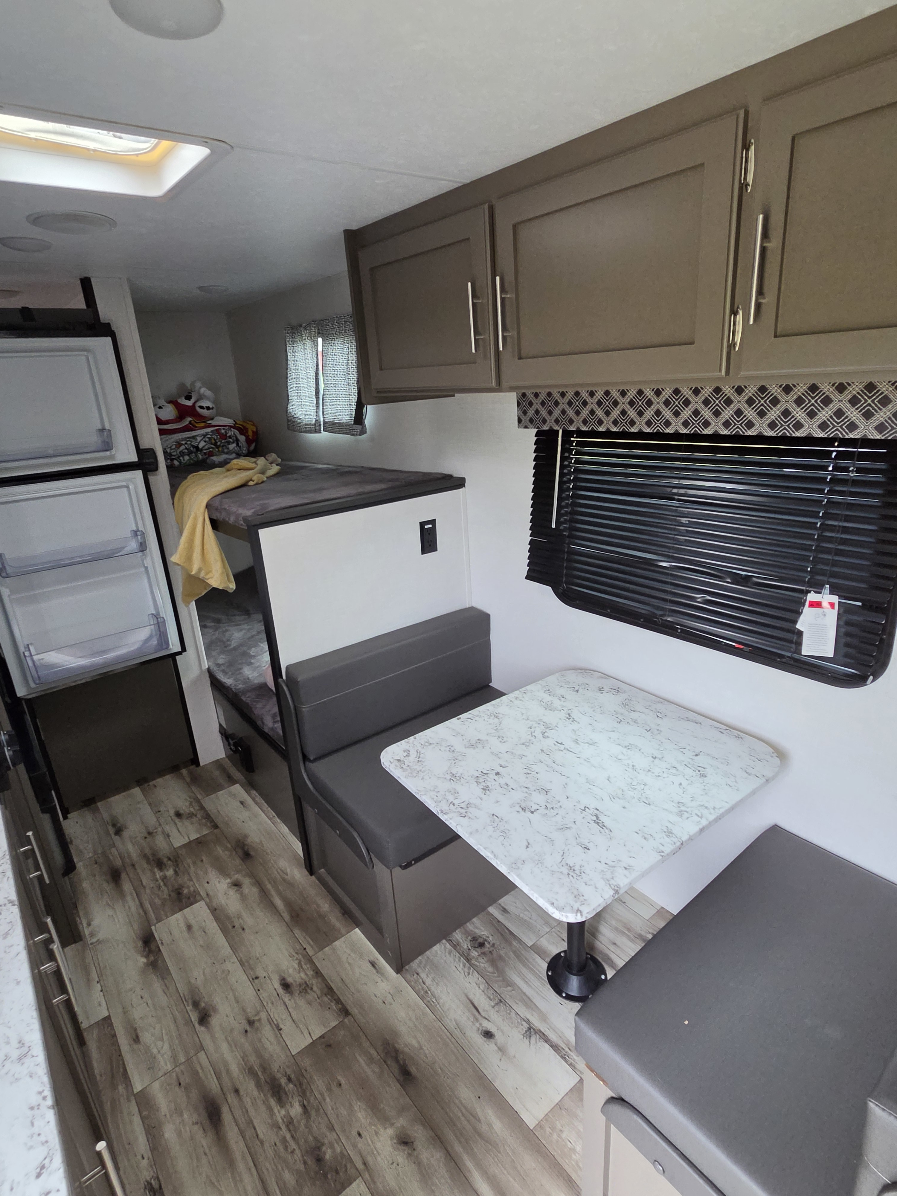 This rv rental's interior features a dinette with bench seating, bunk beds, an open fridge, and overhead cabinets.. KZ Sportsmen Classic 2024