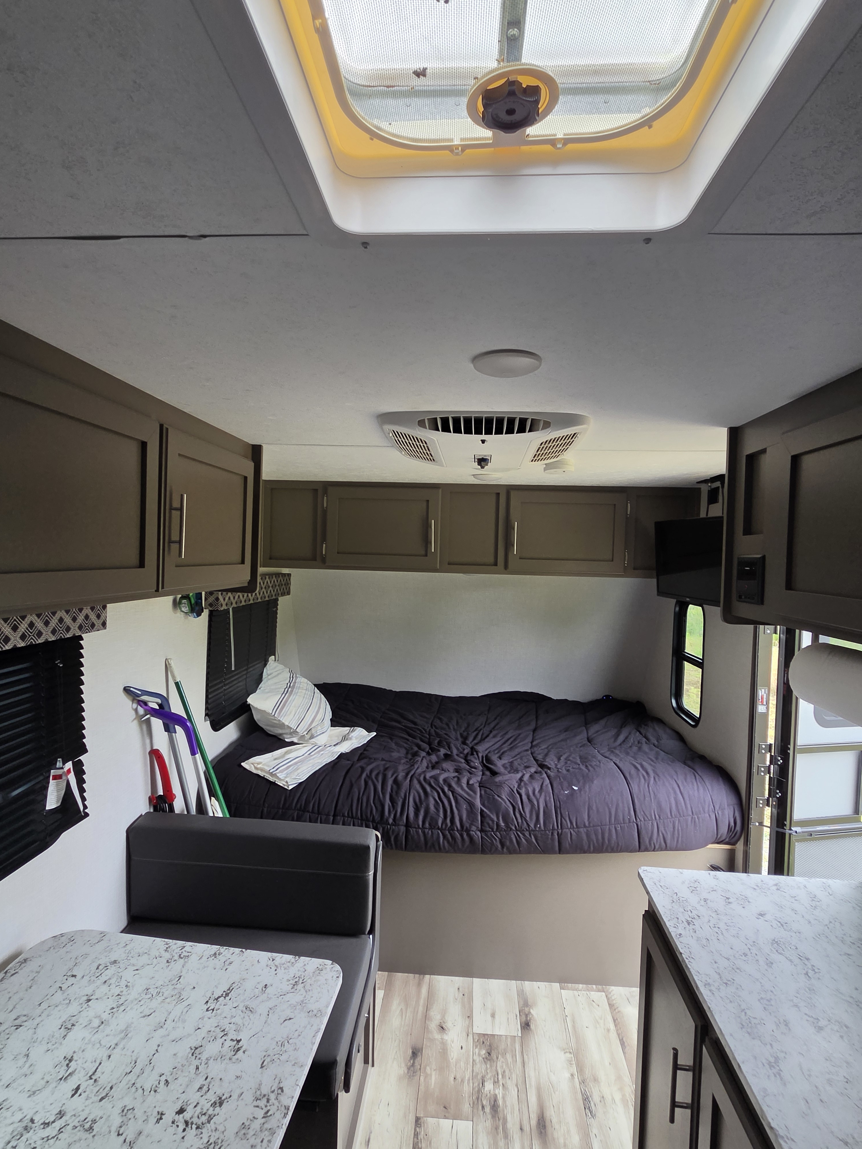 Cozy RV rental interior with a spacious bed, dinette seating, kitchen counter, overhead cabinets, and an AC unit.. KZ Sportsmen Classic 2024