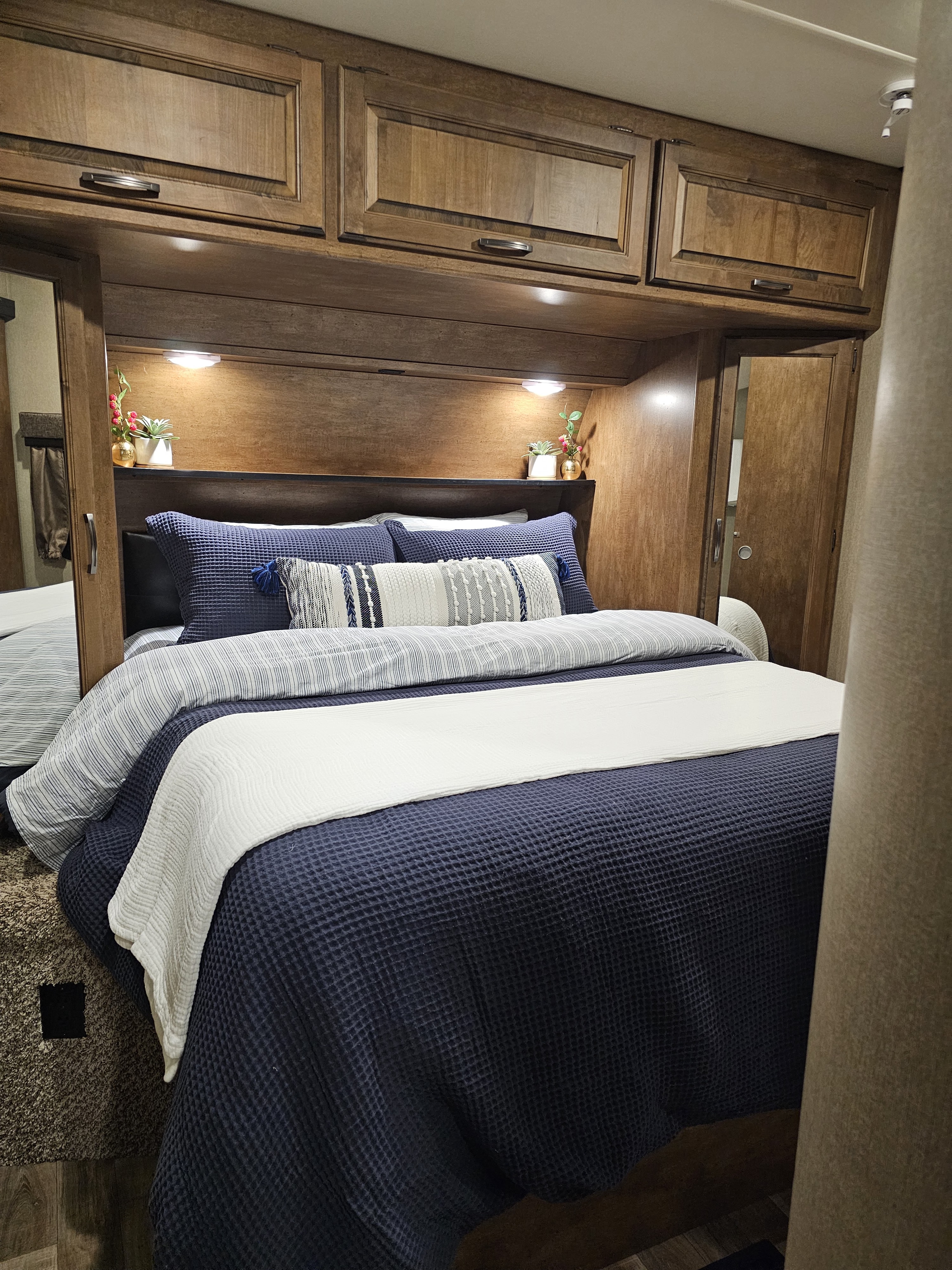 Cozy RV rental bedroom with dark wood cabinets, blue bedding, and soft lighting for a comfortable stay.. Grand Design Reflection 2016