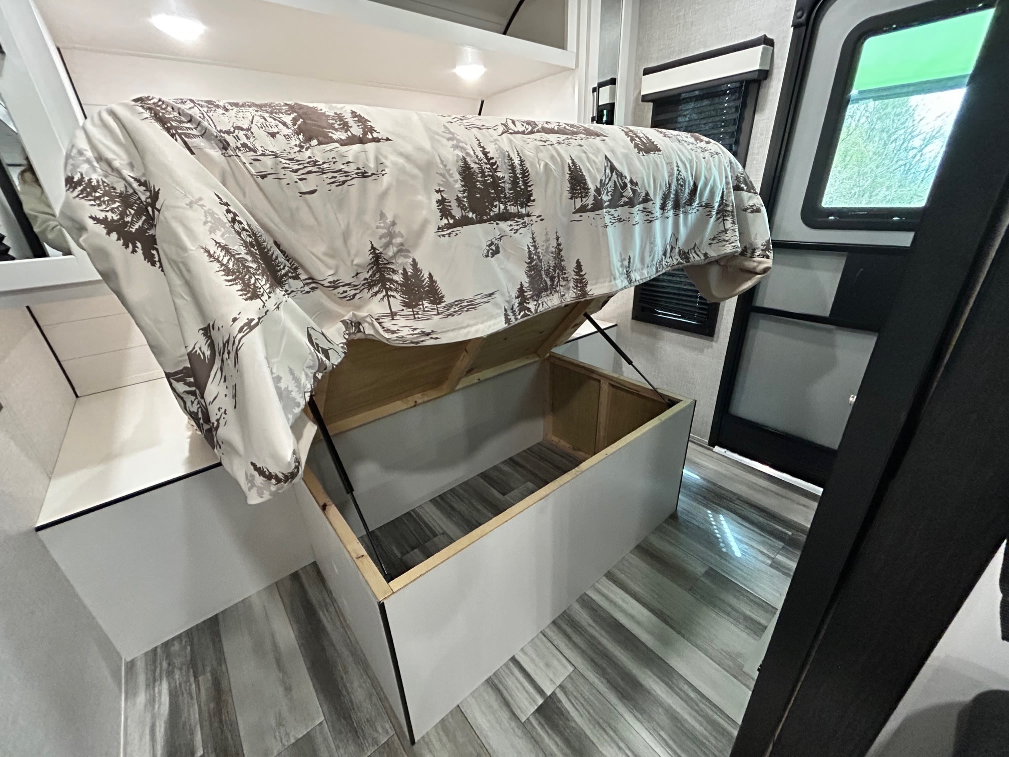 RV rental bed lifted, revealing under-bed storage. Features a forest-patterned comforter & compact interior. Ideal for trips.. Jayco Jay Flight 2024