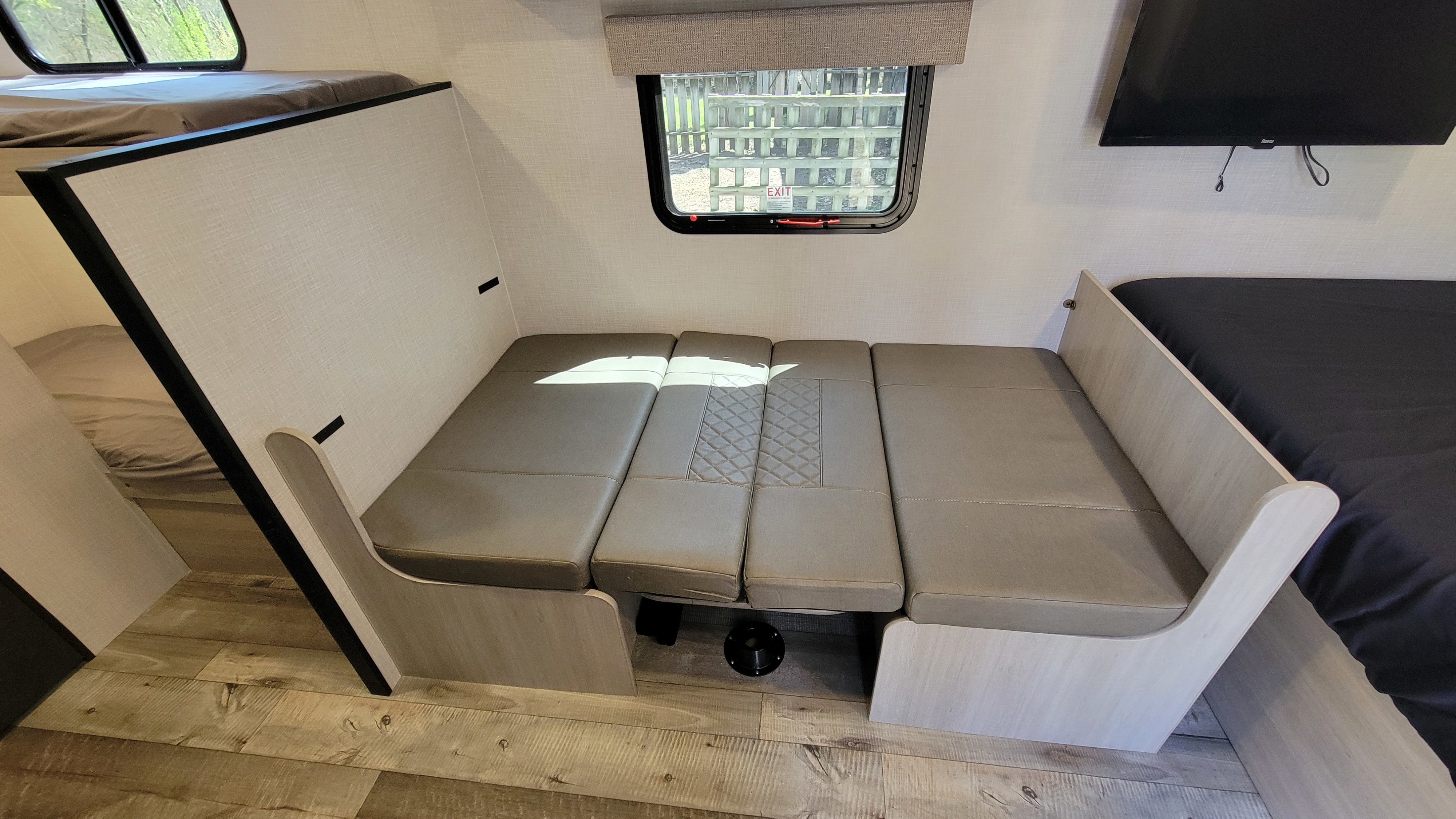 RV rental interior: A light-toned dinette area converts to a bed, flanked by bunk beds (left) and another bed with TV (right).. Crossroads RV Sunset Trail 2026