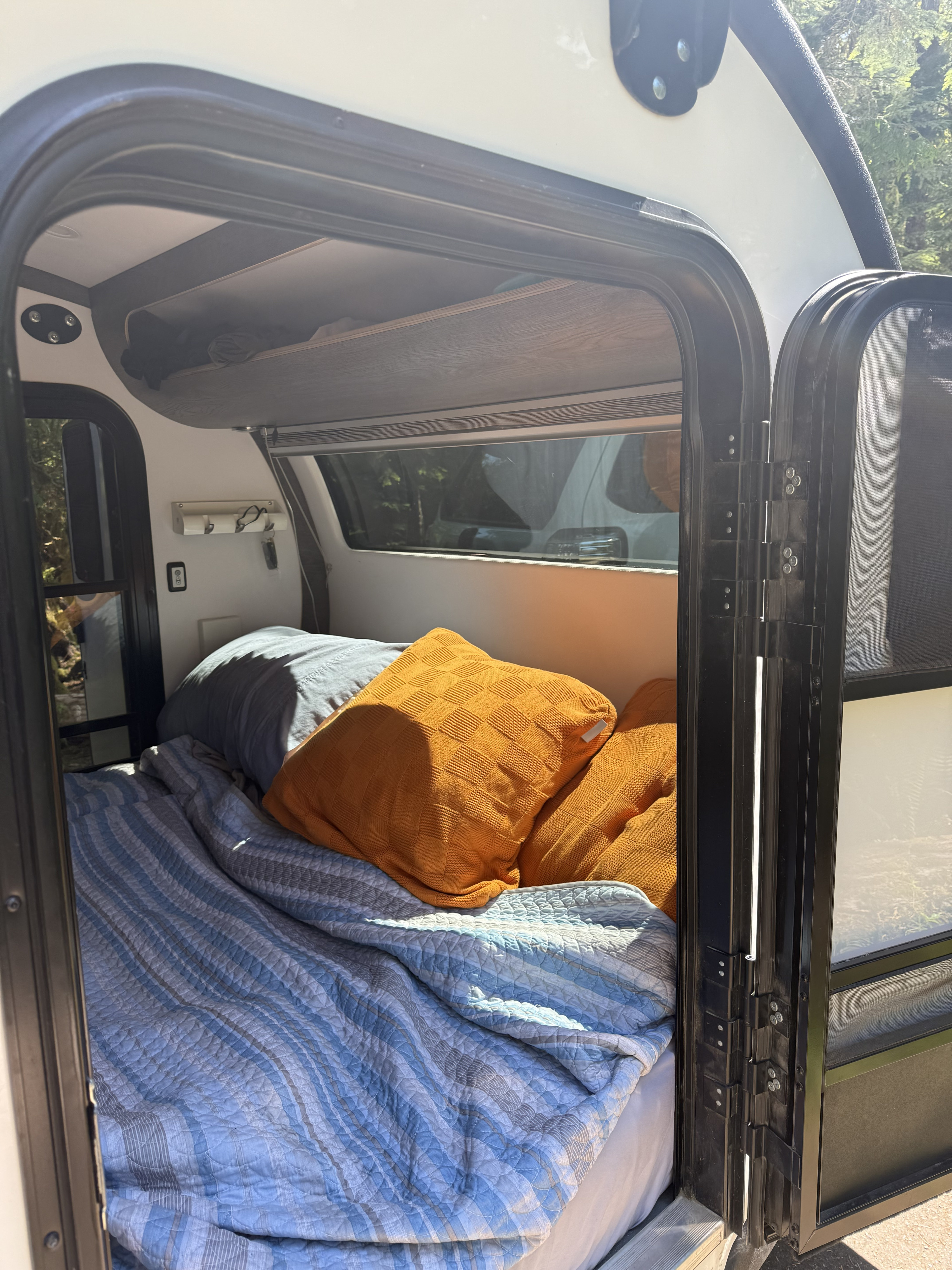 Cozy RV rental interior: a comfortable sleeping area with blue and orange pillows, visible through the open doorway of the camper.. Bean Trailer Bean Stock 1.0 2022