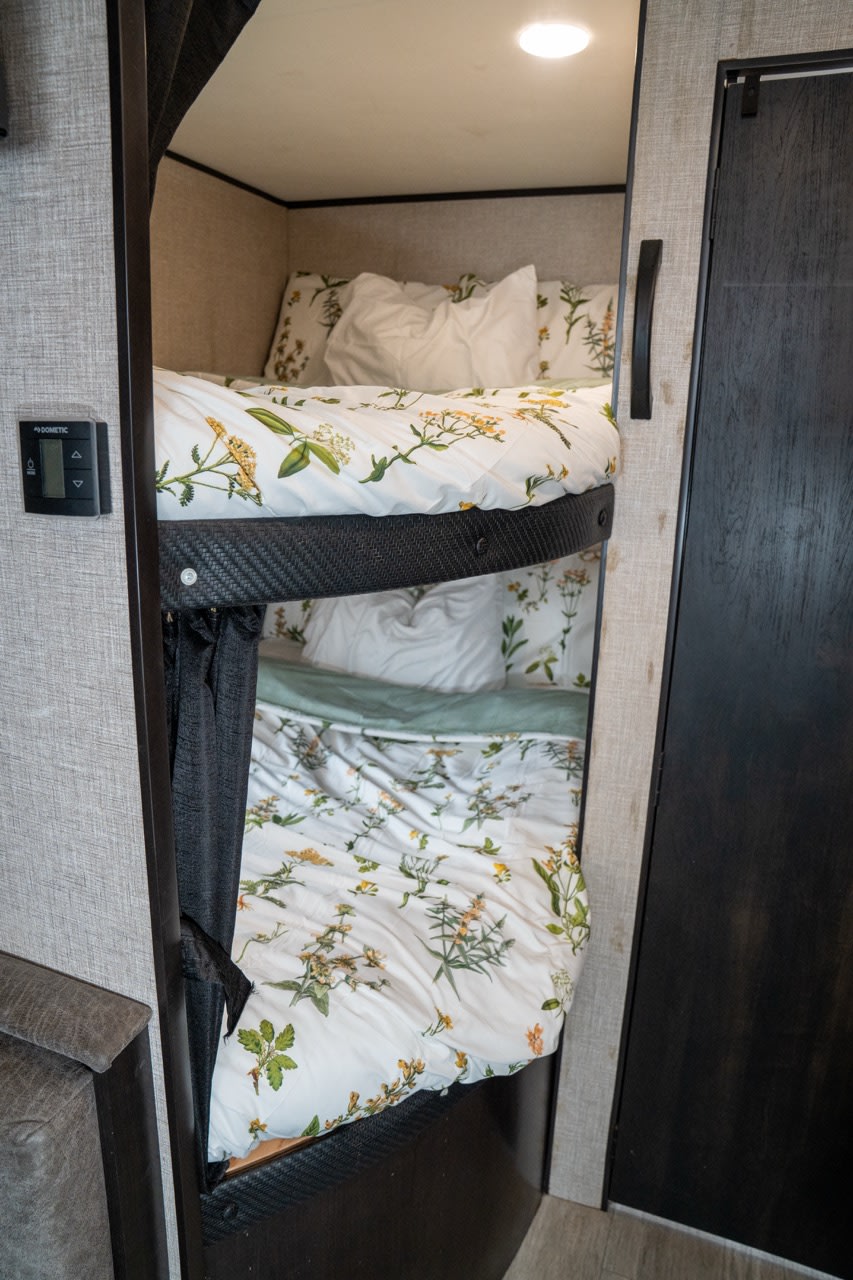 An RV rental's cozy bunk beds with floral bedding, a privacy curtain, and a Dometic control panel.. Jayco Jay Flight SLX 2021