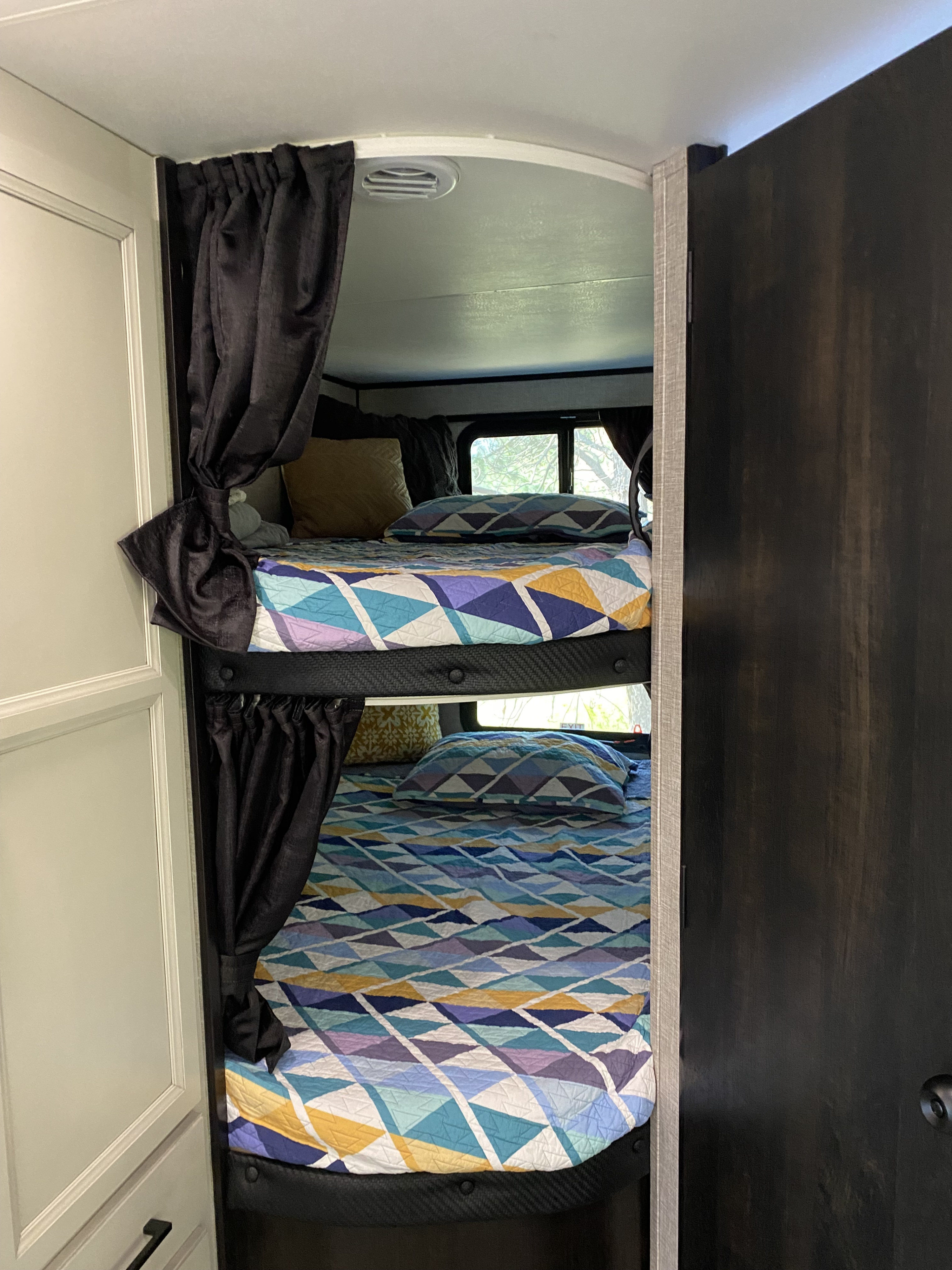 RV rental bunk beds with vibrant geometric quilts and privacy curtains, providing cozy sleeping quarters in a camper.. Jayco Jay Flight 2023