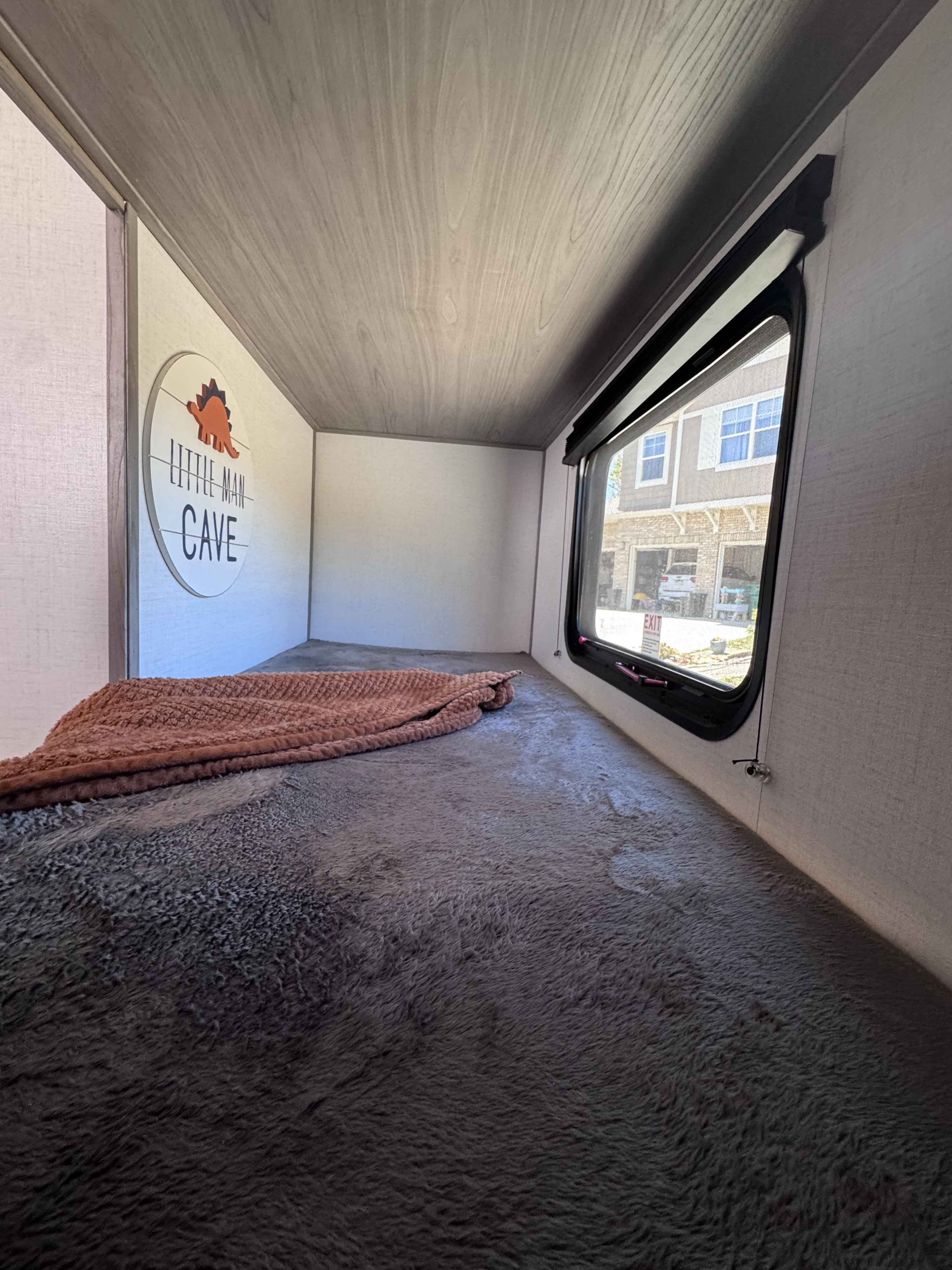 RV rental bunk bed: a cozy sleeping area with fluffy gray bedding, a "Little Man Cave" sign, and window view.. Dutchmen Coleman Lantern LT 17b 2024