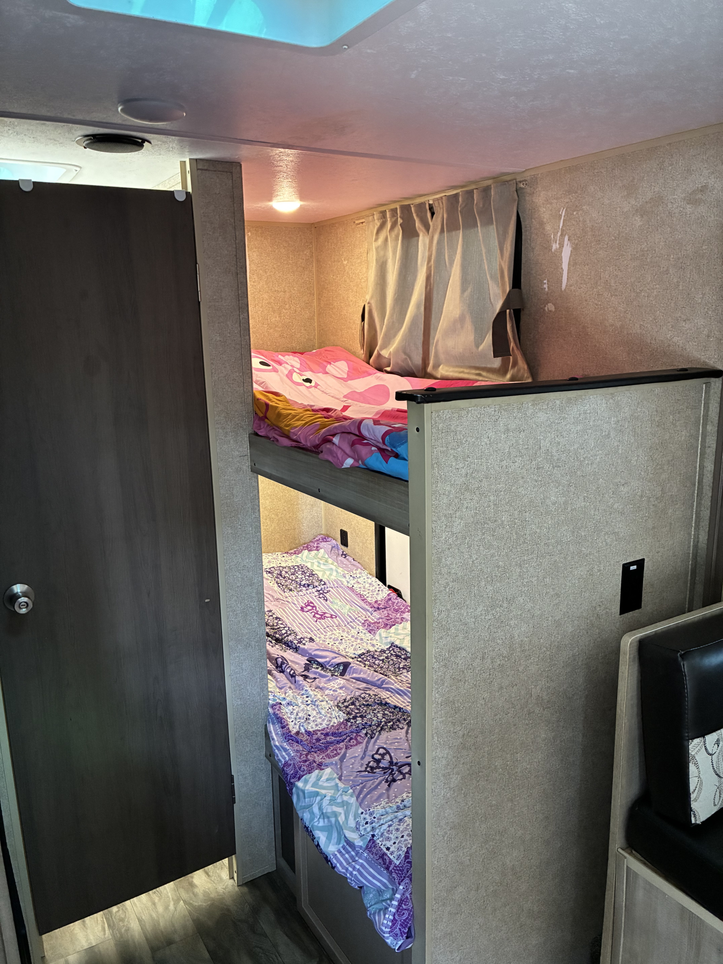 An RV rental interior featuring two bunk beds with pink and purple bedding, a door, and a cozy sleeping area.. Coachmen Catalina Sumit Series 2019