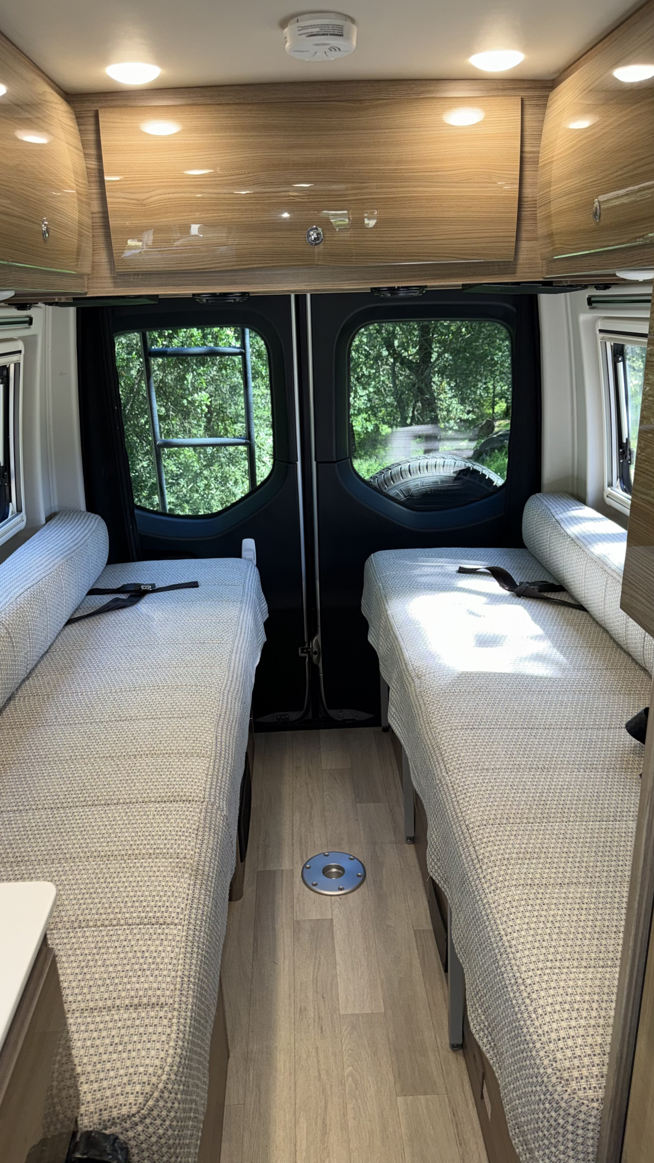 Bright RV rental interior with wood cabinets, two beds/benches with seatbelts, and outdoor views from rear windows.. Winnebago Boldt 2020