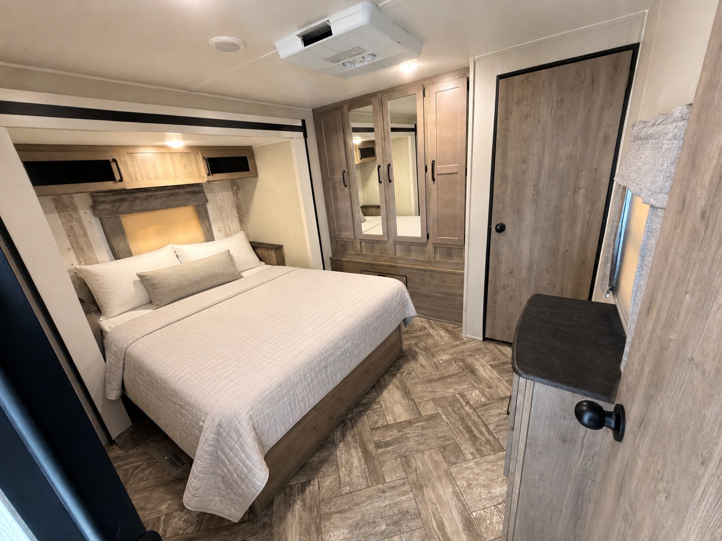 Cozy RV rental bedroom with modern wood finishes, a large bed, overhead cabinets, and mirrored closet doors.. Forest River Puma 2023