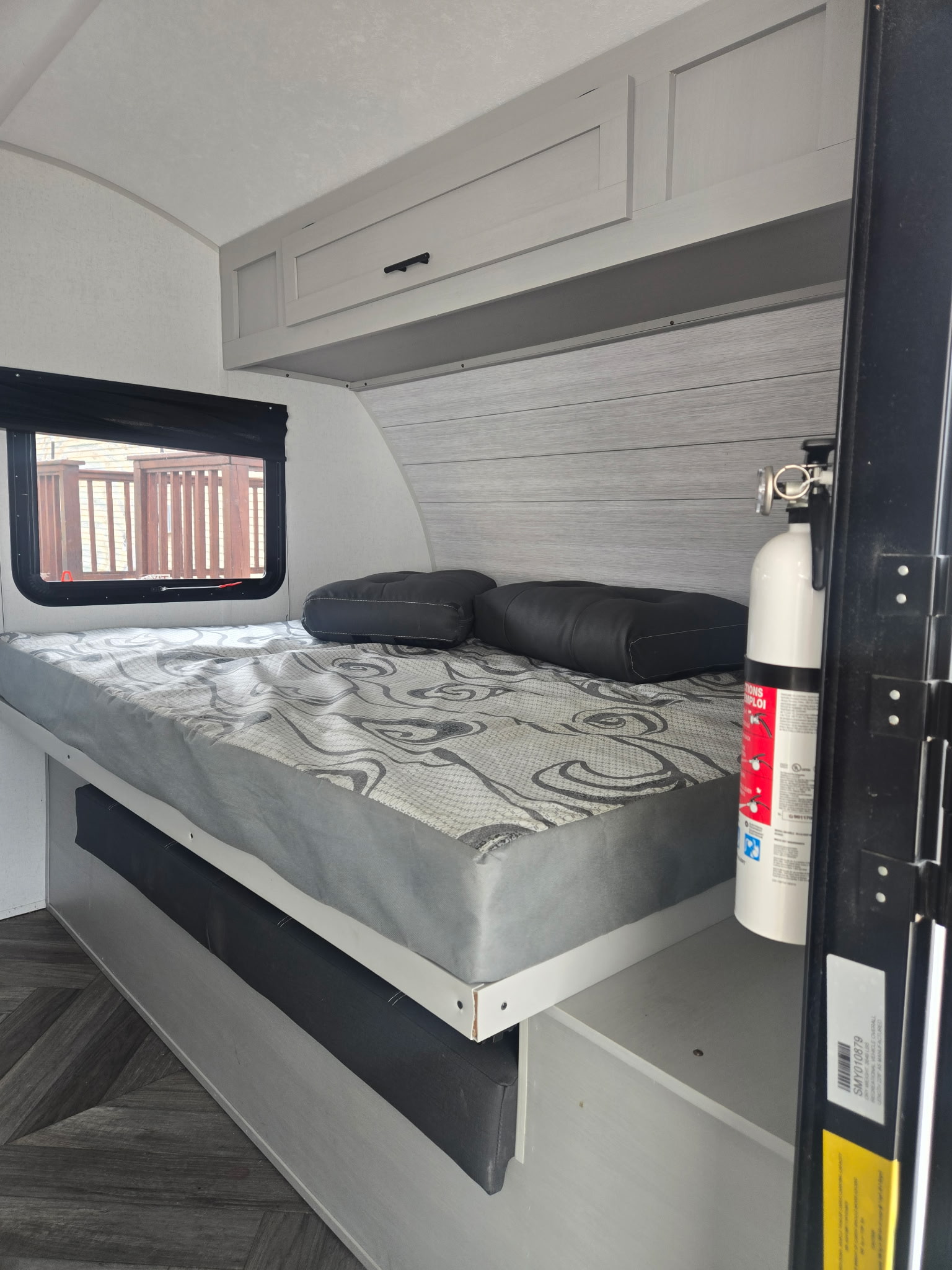Compact RV rental bedroom showing a bed with pillows, window, overhead cabinets, and a fire extinguisher near the entry.. Forest River Salem FSX 2022