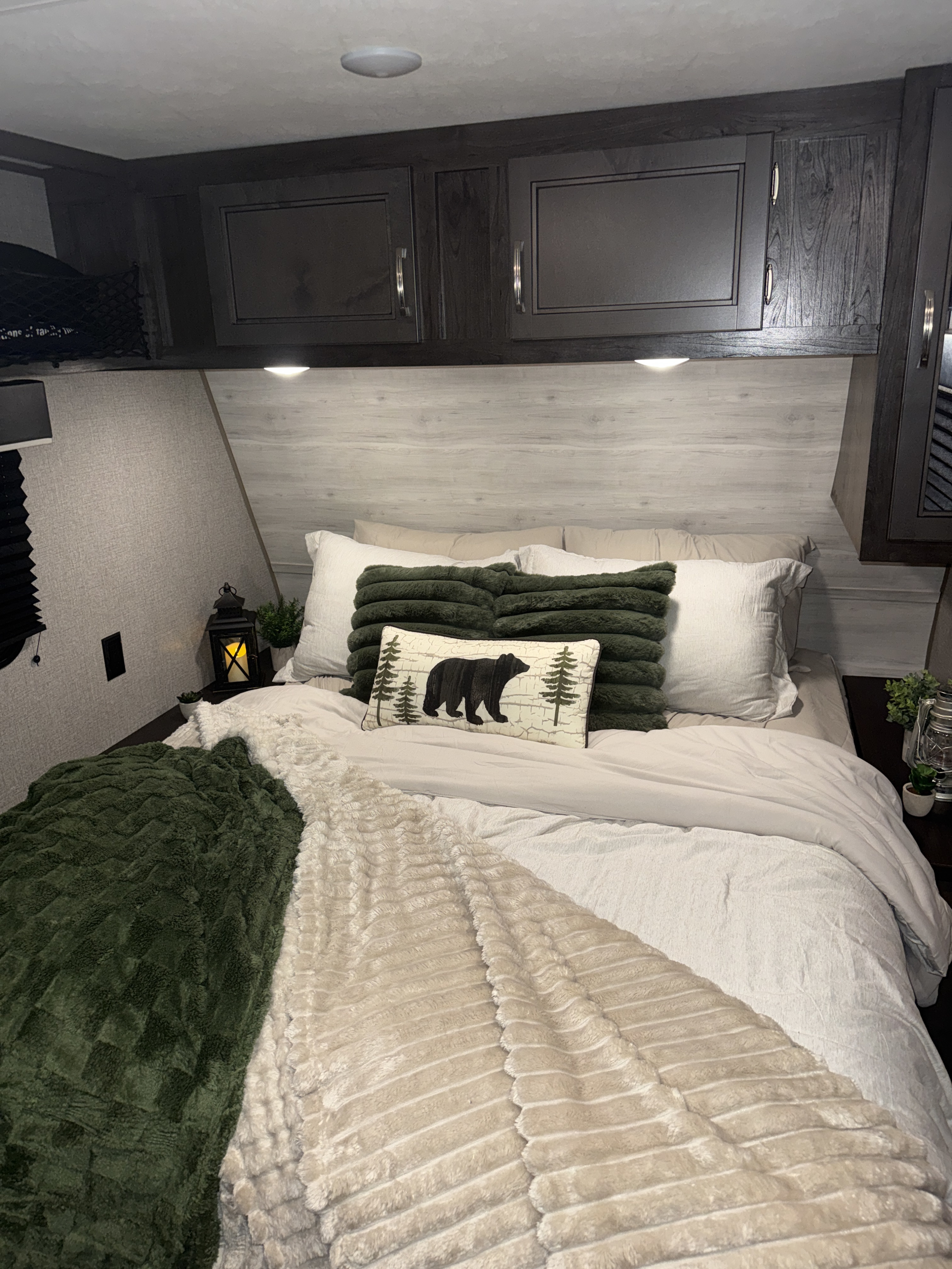 Cozy RV rental bedroom with a bear-themed pillow, plush blankets, overhead storage, and bedside decor like a lantern.. Jayco Jay Flight SLX 2021