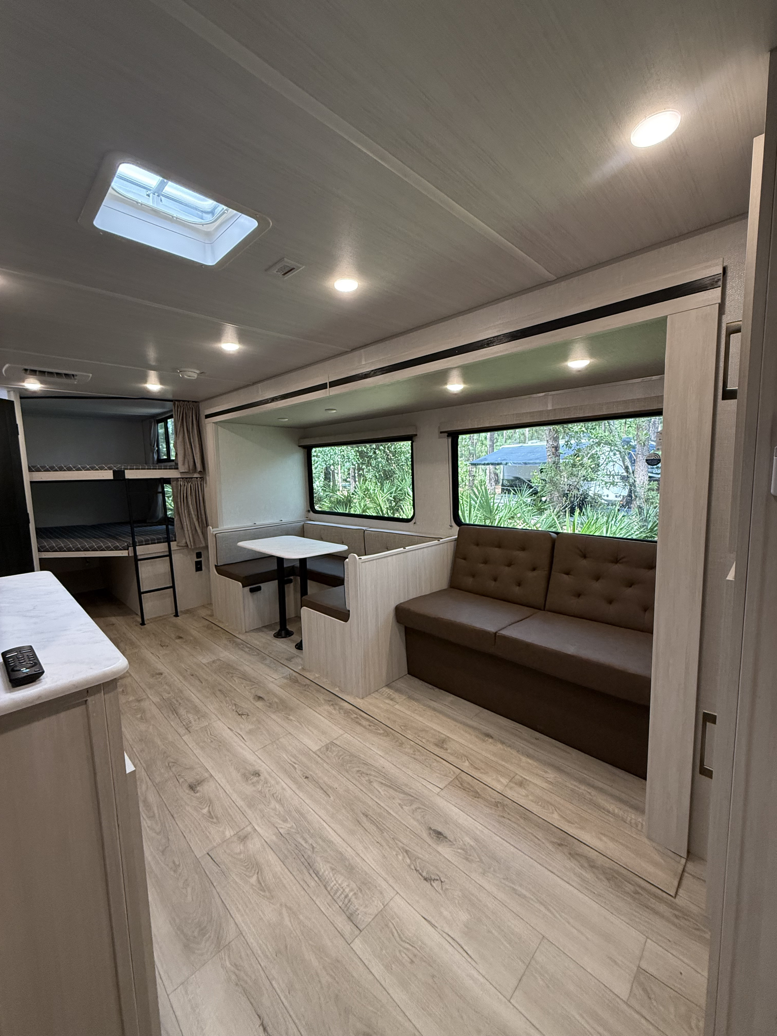 Modern RV rental interior with light wood floors, bunk beds, a dinette, and a comfy sofa. Ideal for family adventures.. Forest River Surveyor Legend X 2025
