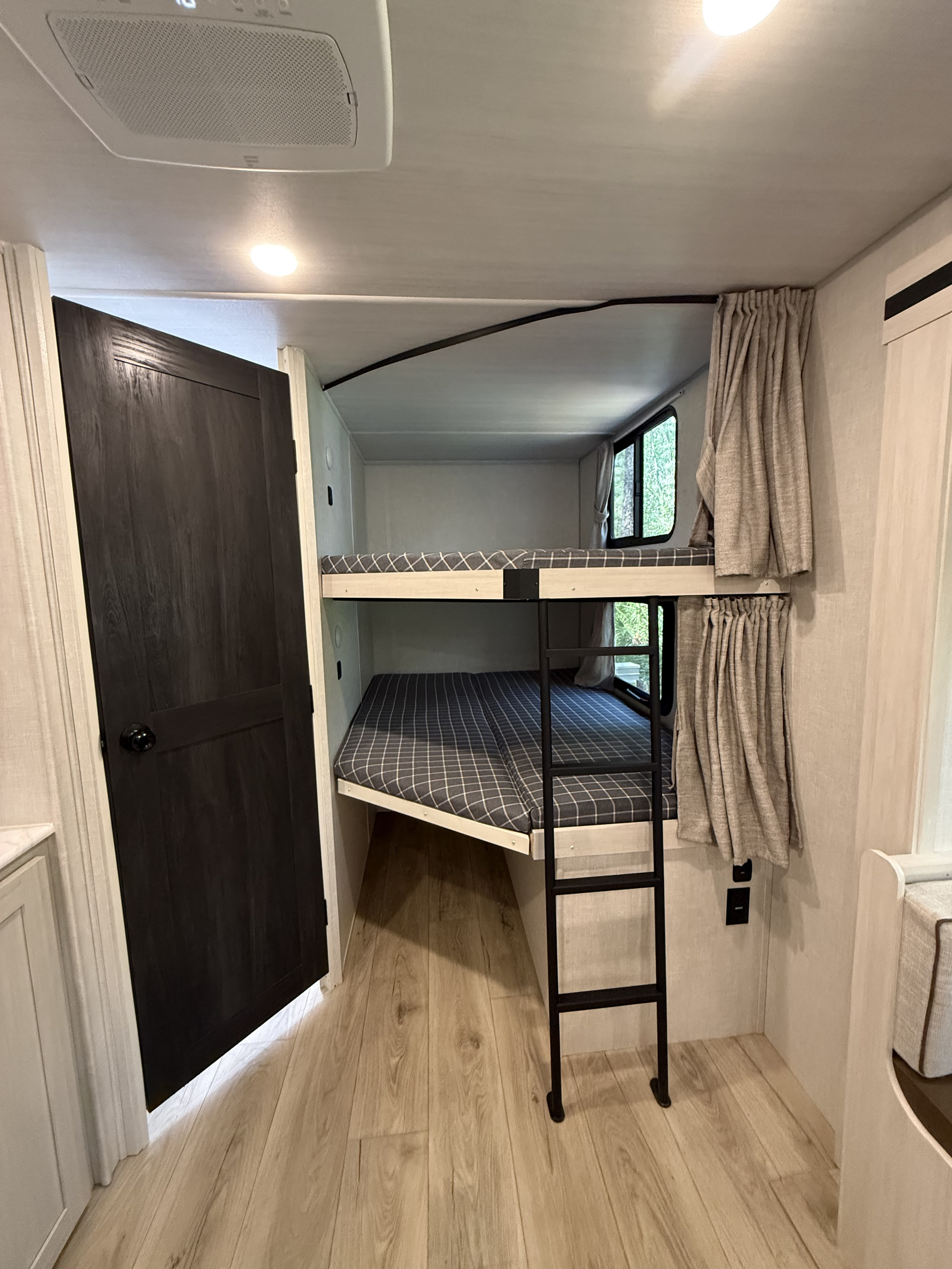 Cozy bunk beds with checkered mattresses in an rv rental. Features a black ladder, light wood floor, and a dark door.. Forest River Surveyor Legend X 2025
