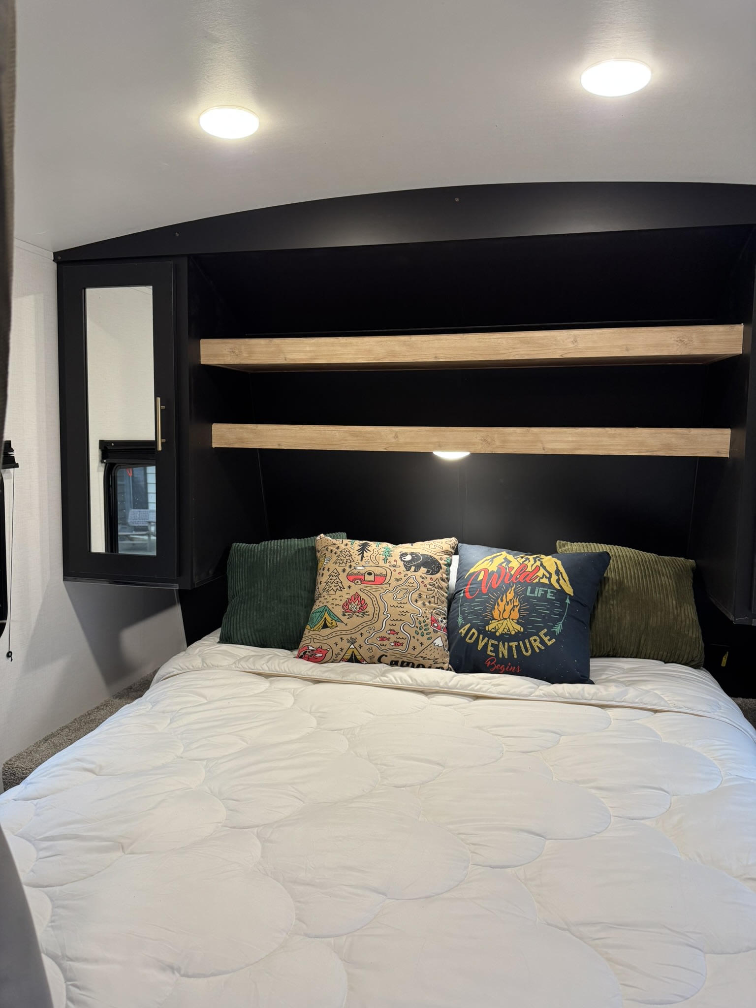 Cozy RV rental bedroom featuring a comfortable bed with decorative throw pillows, built-in shelving, and a mirrored wardrobe.. Keystone RV Springdale 2022
