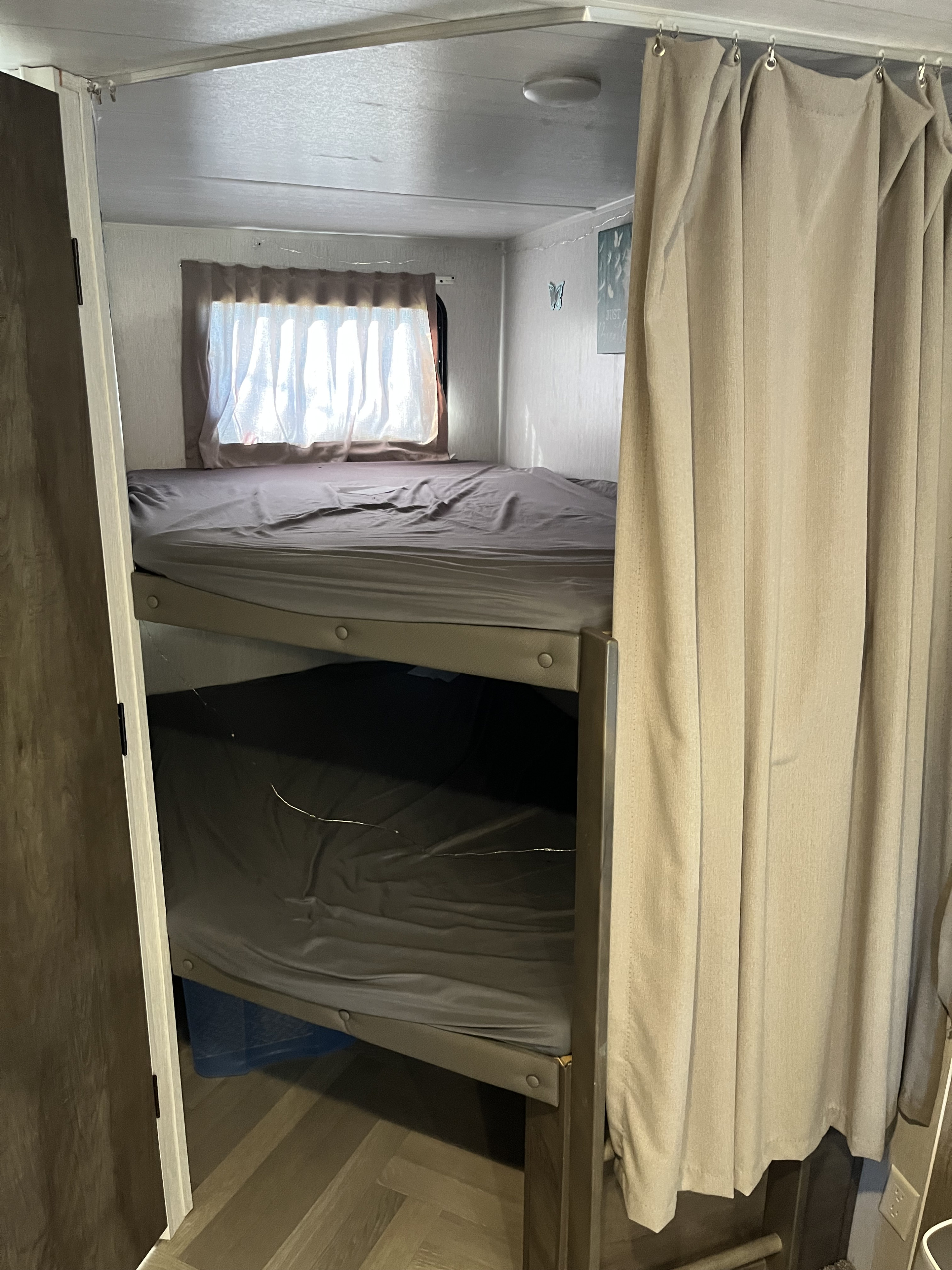 Inside an RV rental: bunk beds with grey sheets, a window, and a beige privacy curtain on a track. Wood floor visible.. Forest River Wildwood 2022