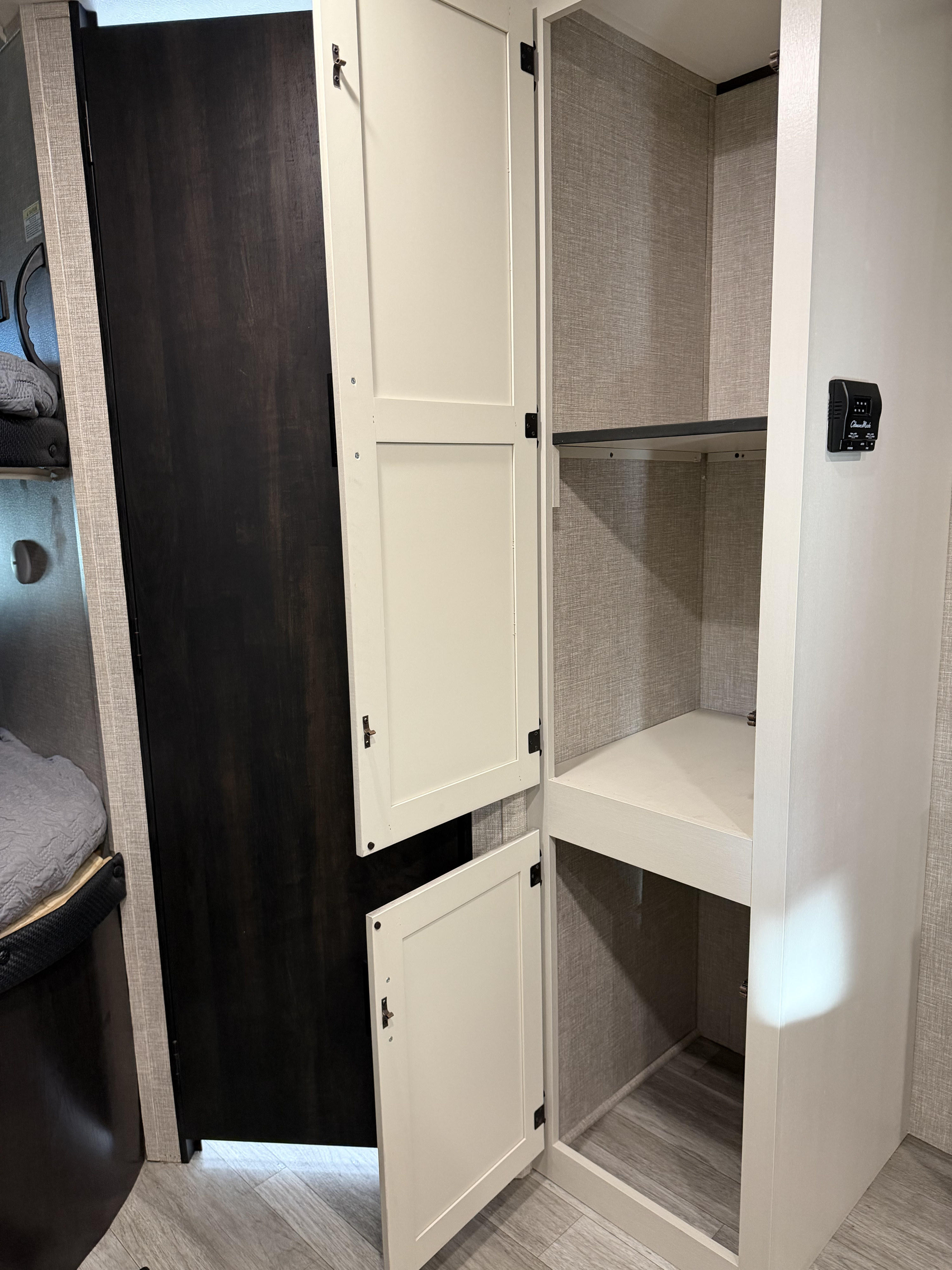 This modern RV rental interior features an open wardrobe with shelving, a bed on the left, and a Climate Master thermostat, offering practical storage.. Jayco Jay Flight Baja Edition 2023