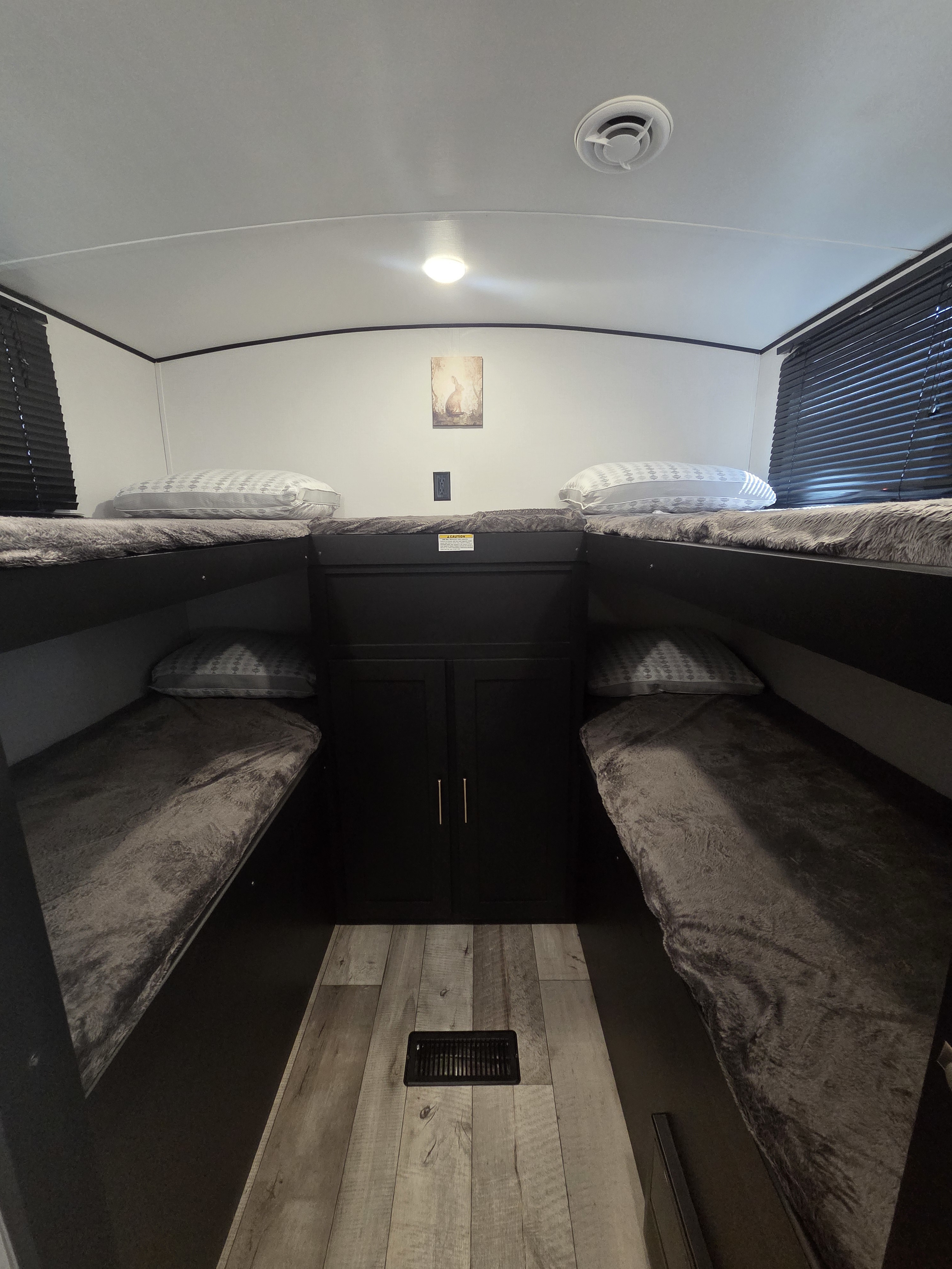 Cozy RV rental bunk room featuring four beds with gray blankets, central cabinet storage, and dark blinds.. Keystone RV Springdale 2022