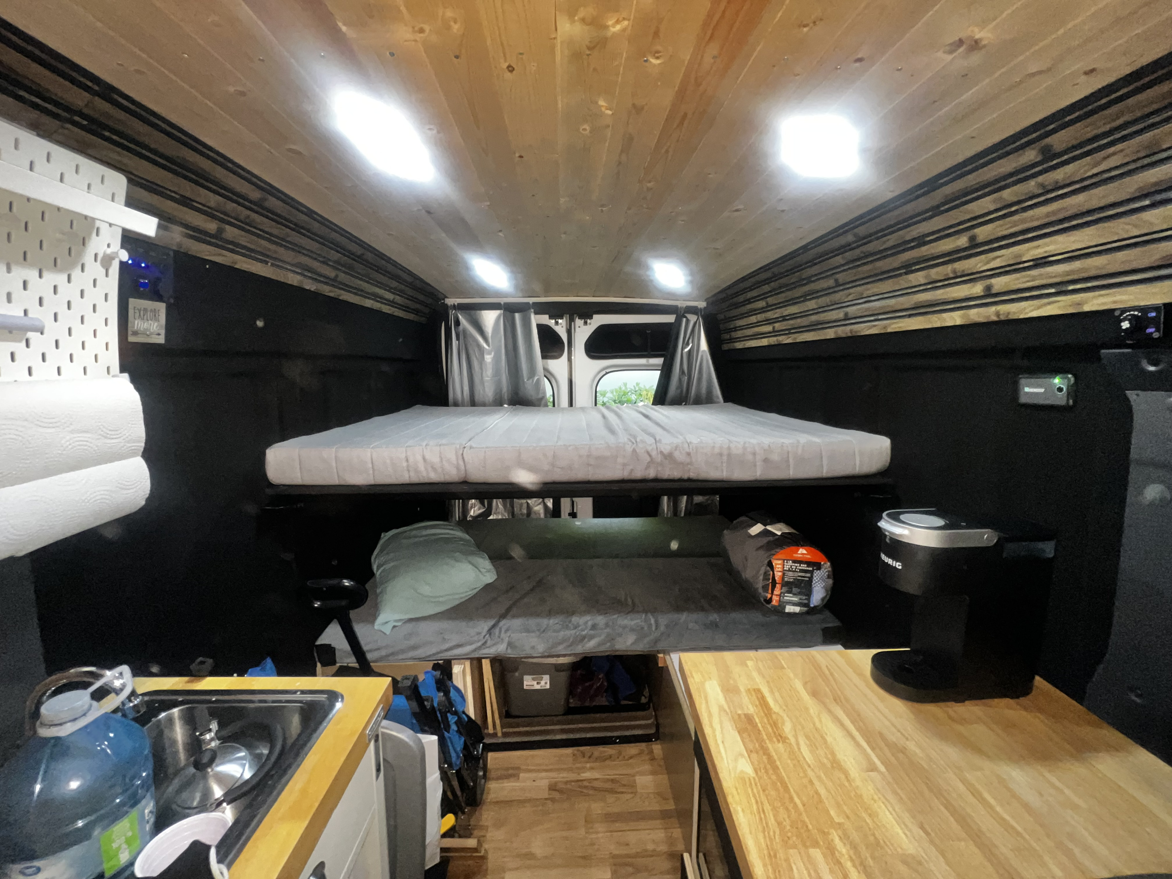 Cozy rv rental camper van interior featuring bunk beds, a compact kitchen, and bright wood-paneled ceiling lights.. Ram Promaster 2019