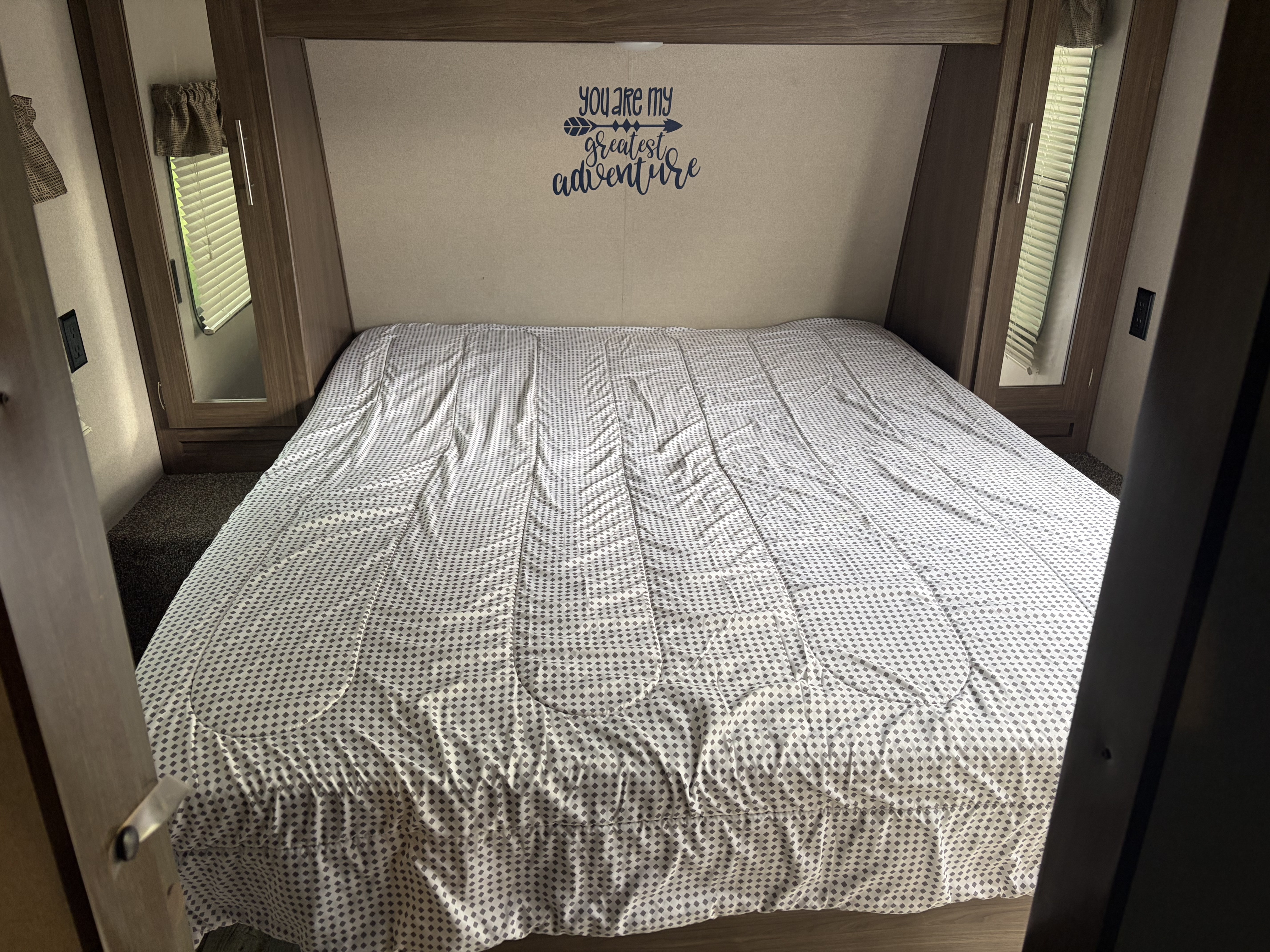 Comfortable RV rental bedroom featuring a patterned bed, built-in storage, and a heartwarming "greatest adventure" decal.. Keystone RV Hideout Luxury 2020