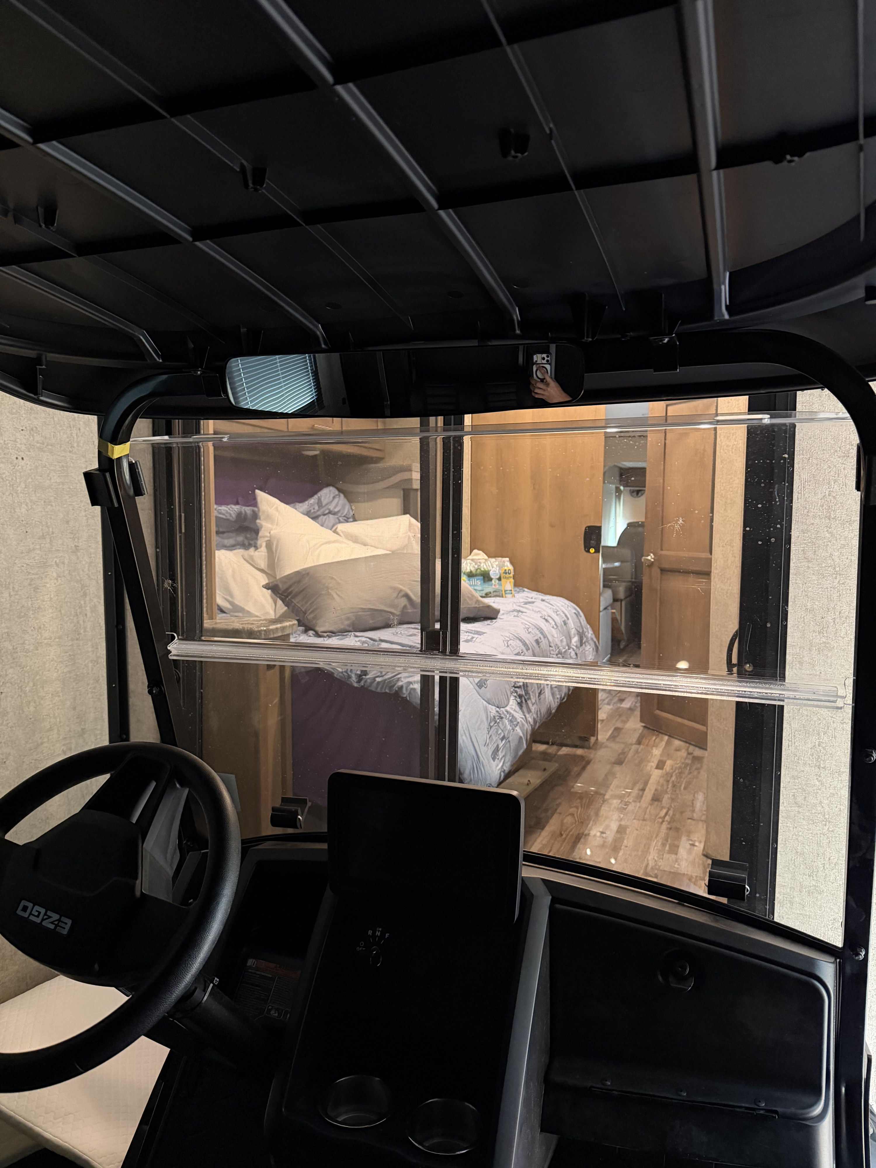 Looking from a golf cart into an RV rental bedroom through the windshield, showing bed, pillows, and steering wheel.. Thor Outlaw 2022