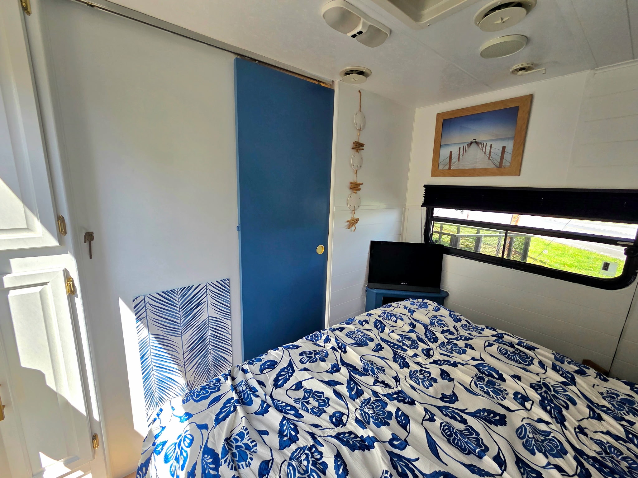 Cozy RV rental bedroom featuring blue floral bedding, a sliding door, and coastal decor. Ideal for a comfortable travel stay.. Sunline Solaris 2002