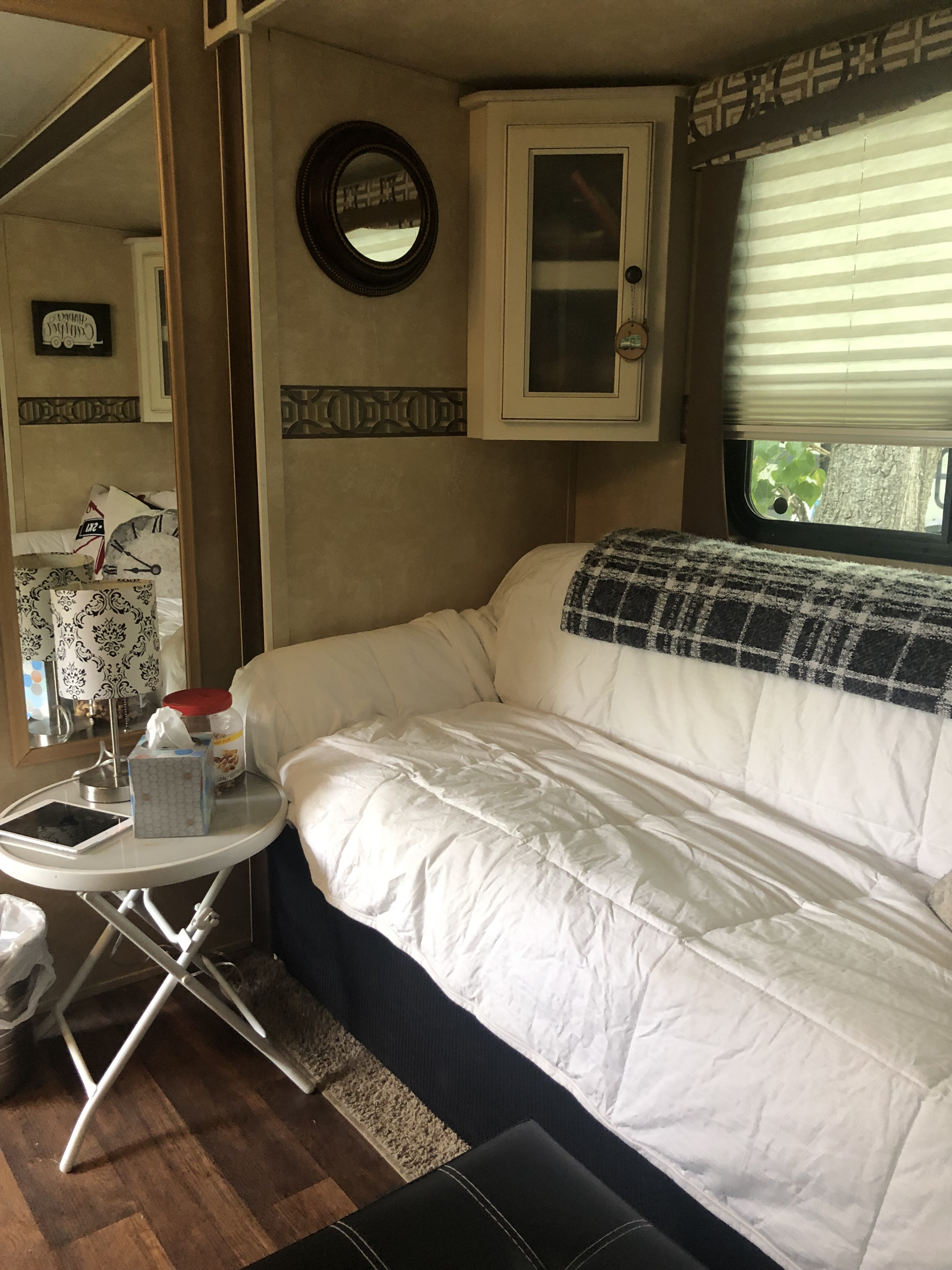 Inviting RV rental interior with a sofa bed, white bedding, plaid blanket, side table, wall mirror, and window view.. Cruiser RV Fun Finder 2013